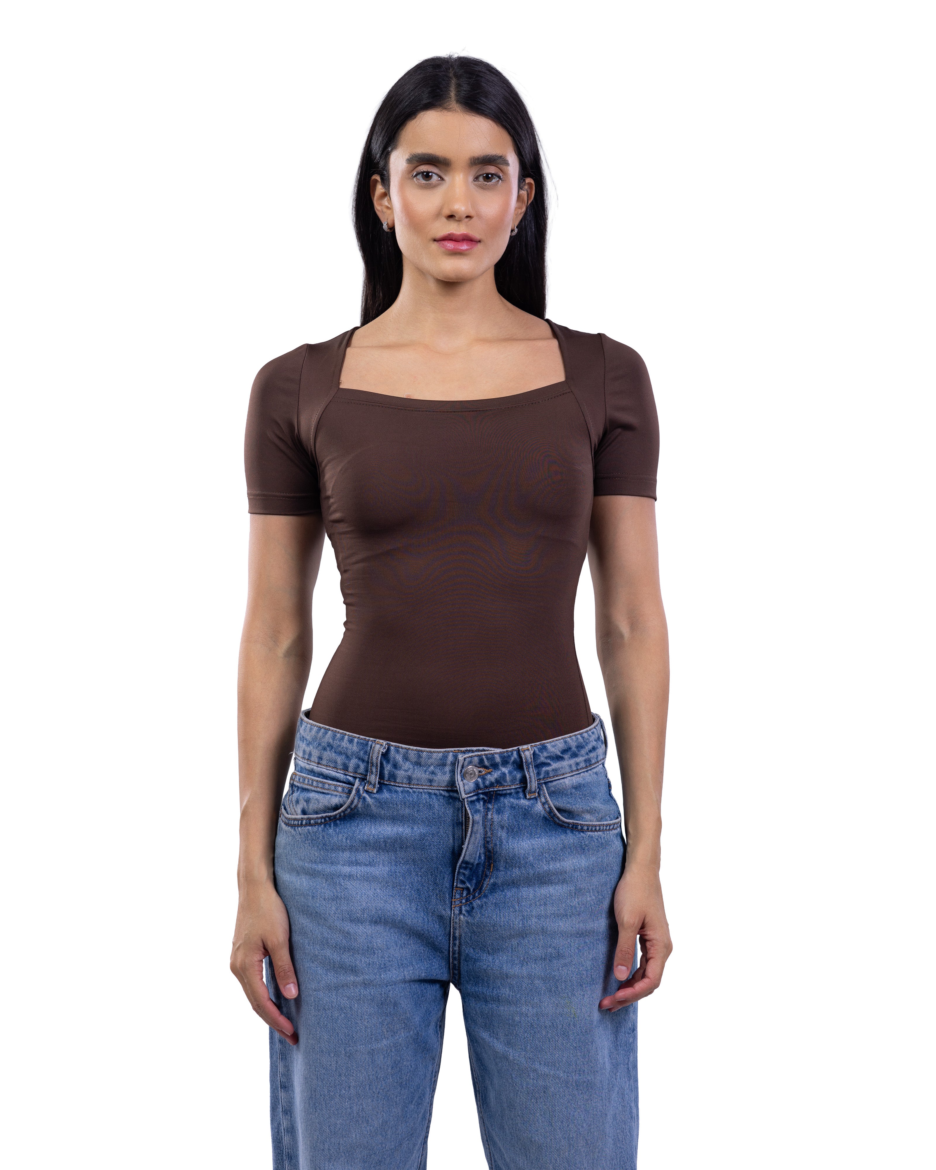 A woman modeling a fitted short-sleeve top with a square neckline in dark brown, paired with blue jeans, against a plain white background.