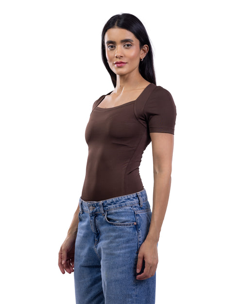 A woman modeling a fitted short-sleeve brown top with a square neckline, paired with blue jeans, against a plain white background.