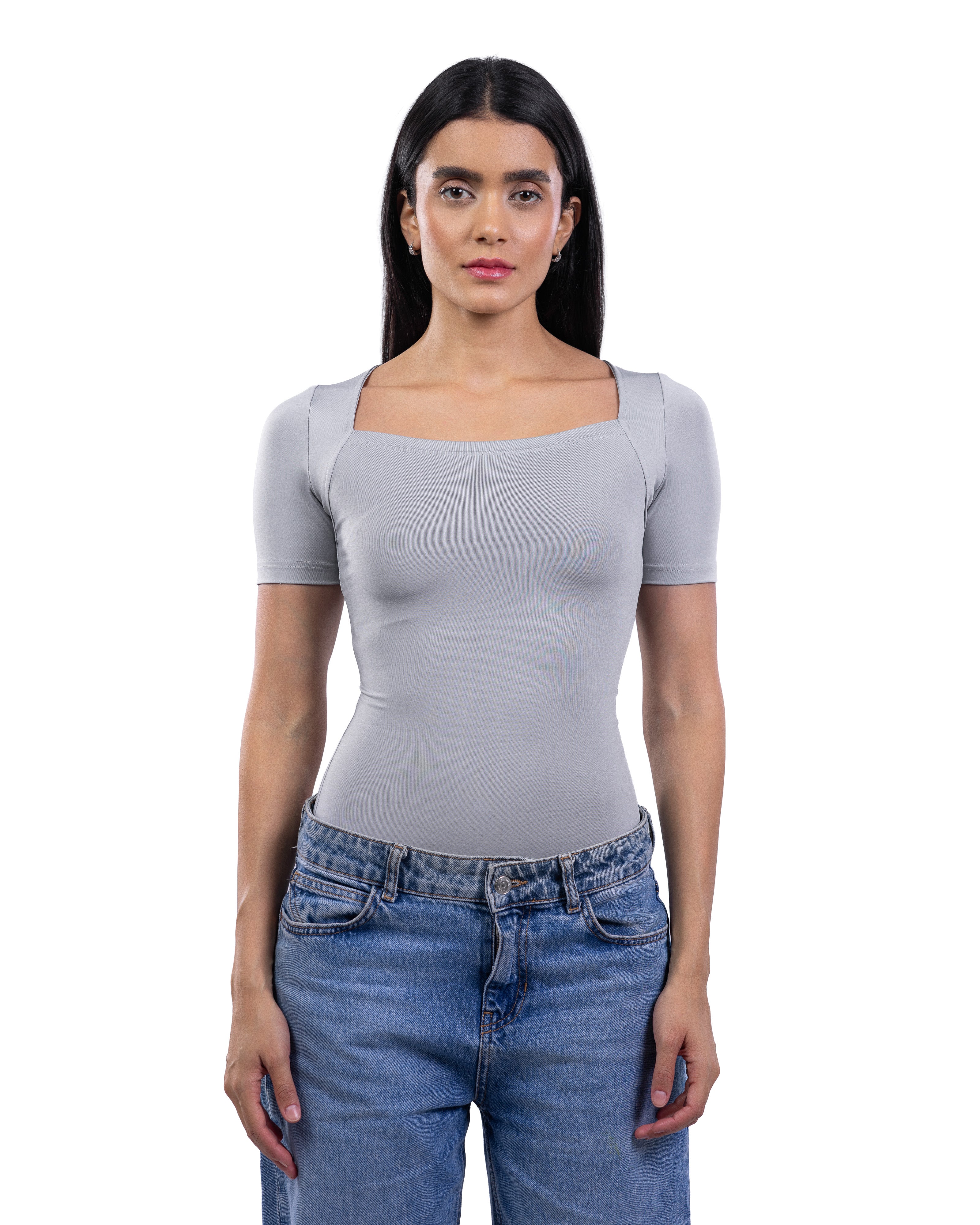 A woman modeling a light gray short-sleeve top with a square neckline, paired with blue jeans, against a plain white background.