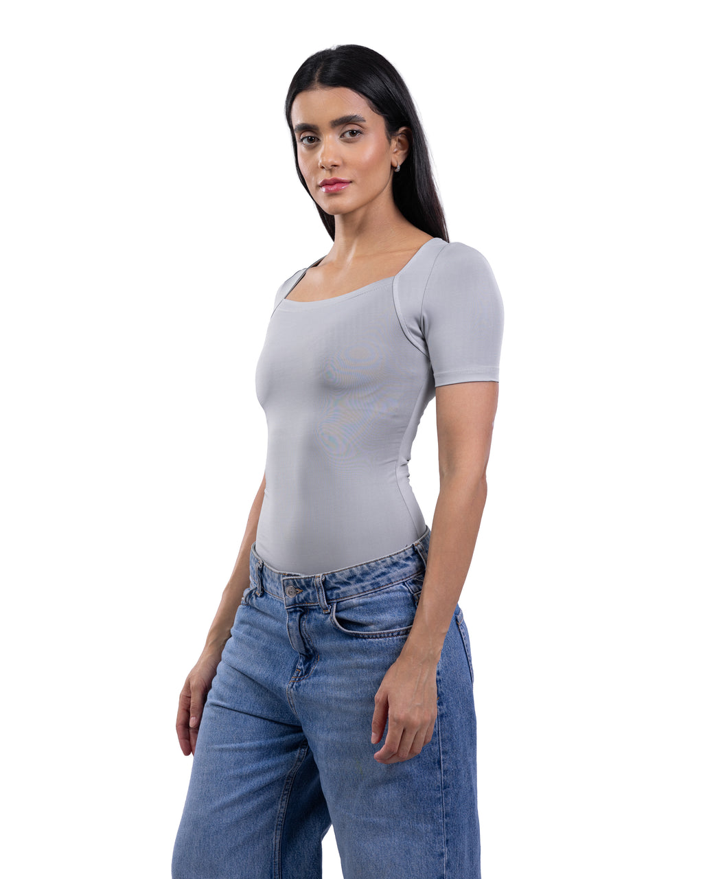 A woman modeling a light gray short-sleeve scoop-neck bodysuit with blue jeans against a plain white background.