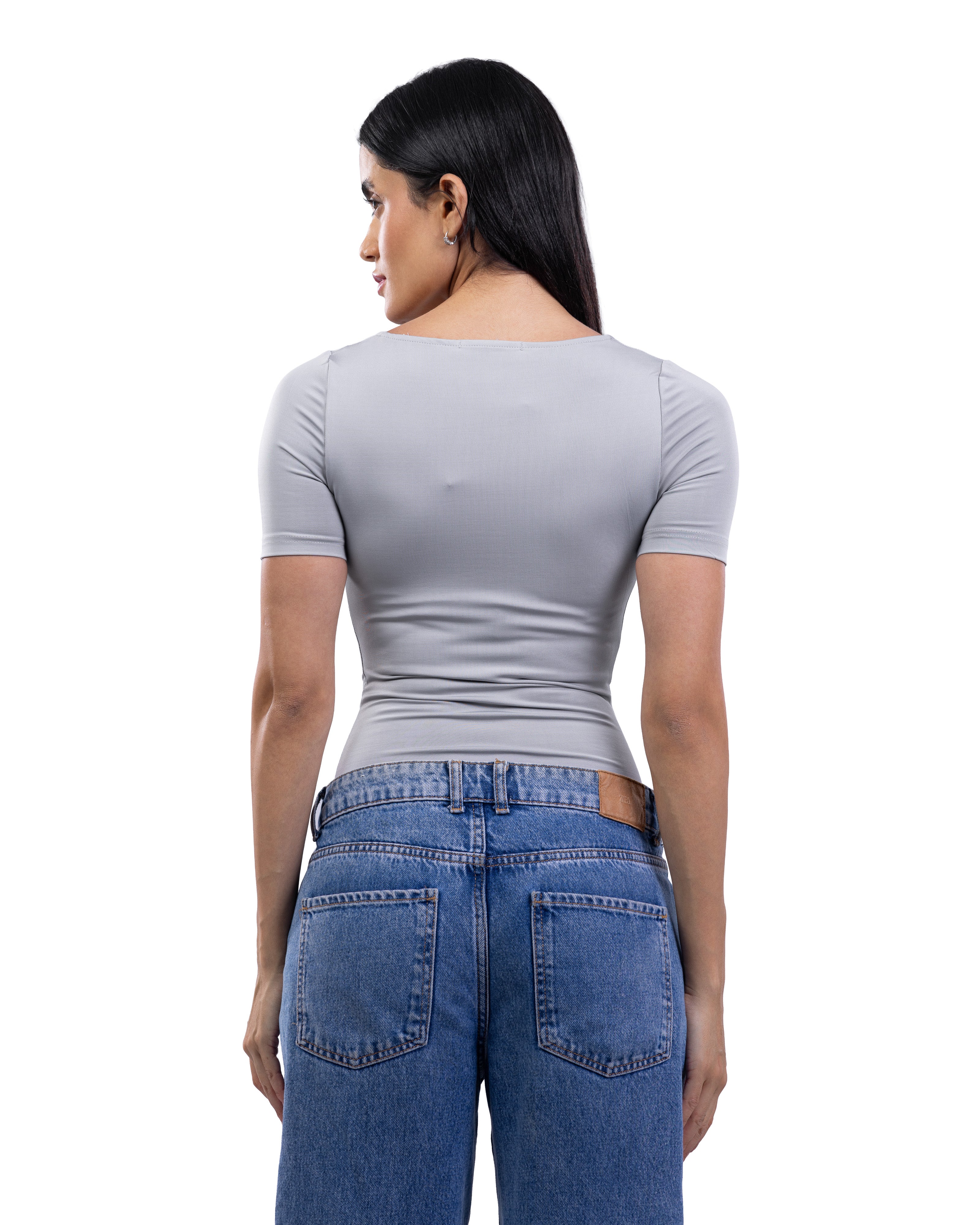 A woman shown from the back wearing a light gray short-sleeve top and blue jeans against a plain white background.