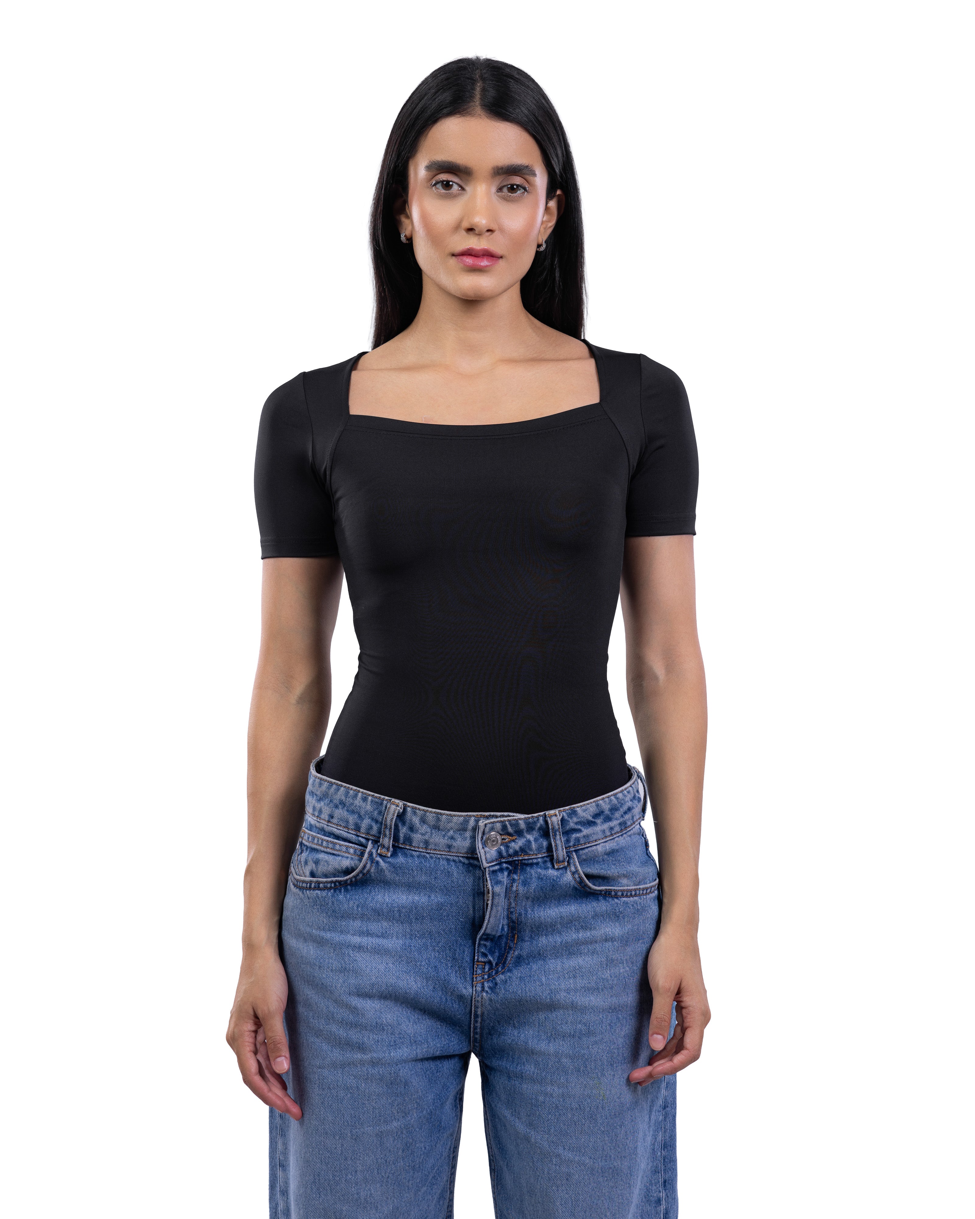 A woman modeling a black short-sleeve top with a square neckline, paired with blue jeans, against a plain white background.