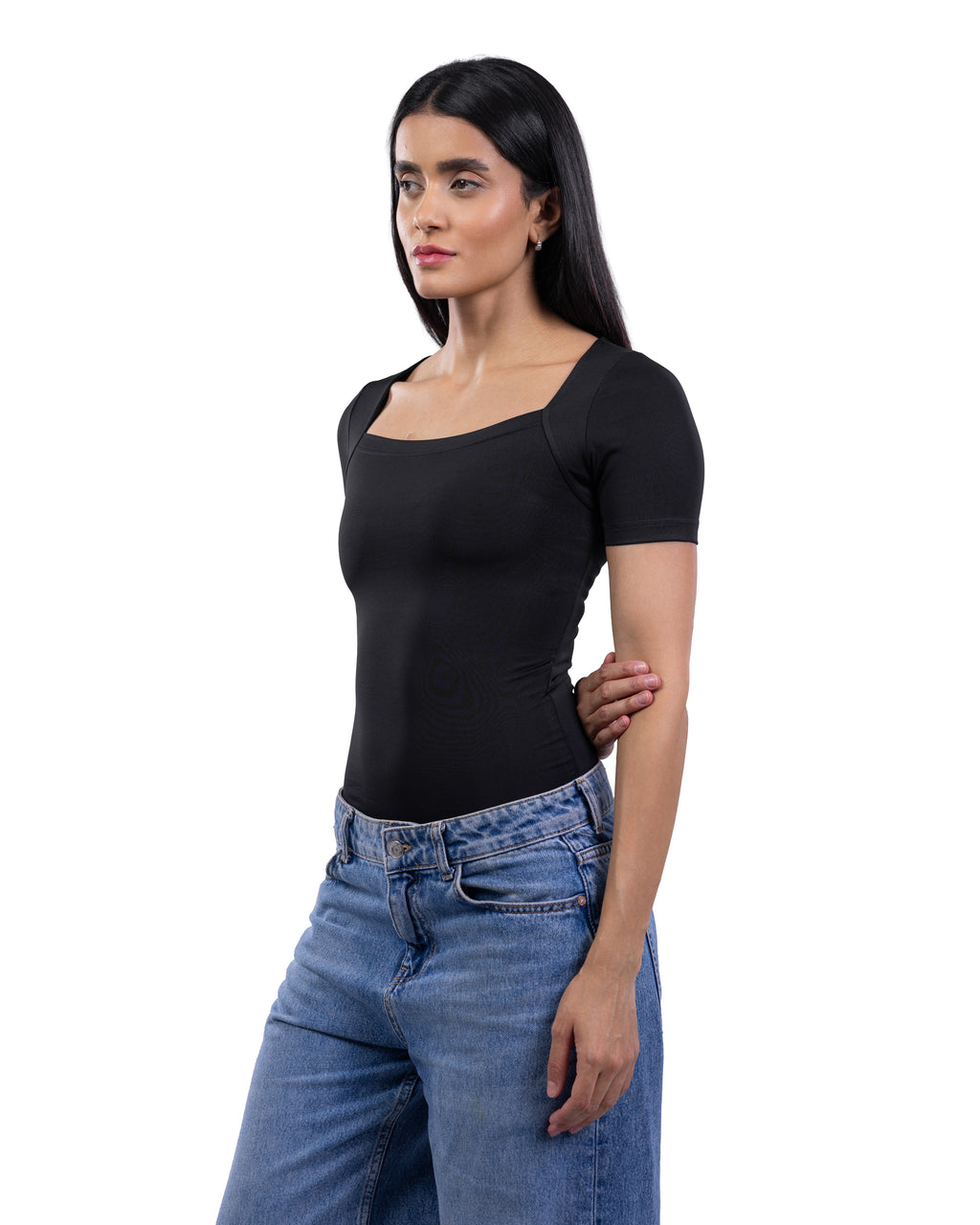 A woman modeling a black short-sleeve scoop-neck top paired with blue jeans, photographed against a plain white studio background.