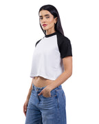 A woman modeling a short-sleeve crop top with a white body and black raglan sleeves, paired with blue jeans, against a plain white background. [model:2]