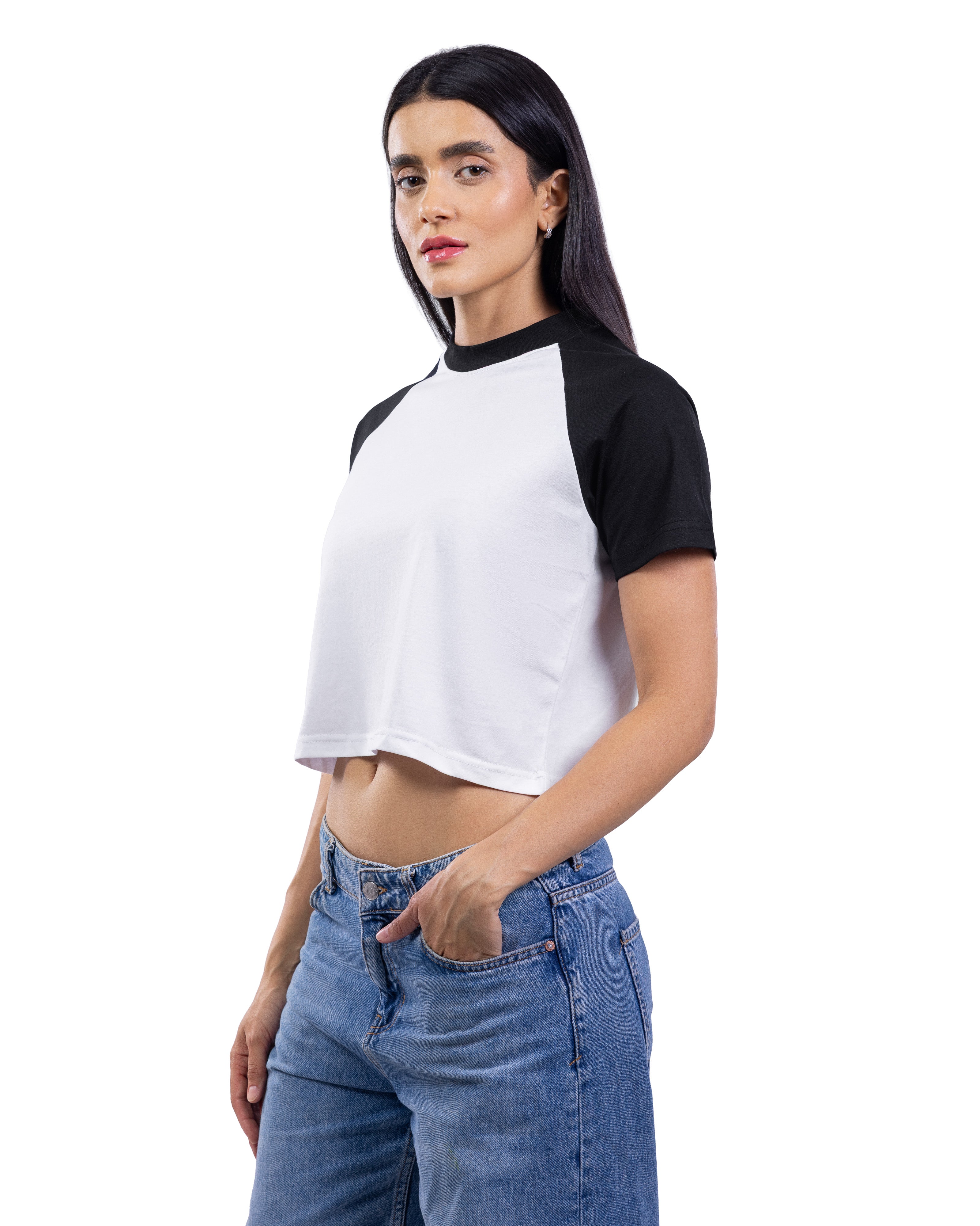 A woman modeling a short-sleeve crop top with a white body and black raglan sleeves, paired with blue jeans, against a plain white background.