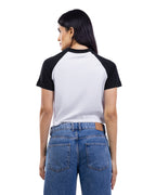 A woman shown from the back wearing a short-sleeve raglan baseball t-shirt with a white body and black sleeves, paired with blue jeans, against a plain white background. [model:2]