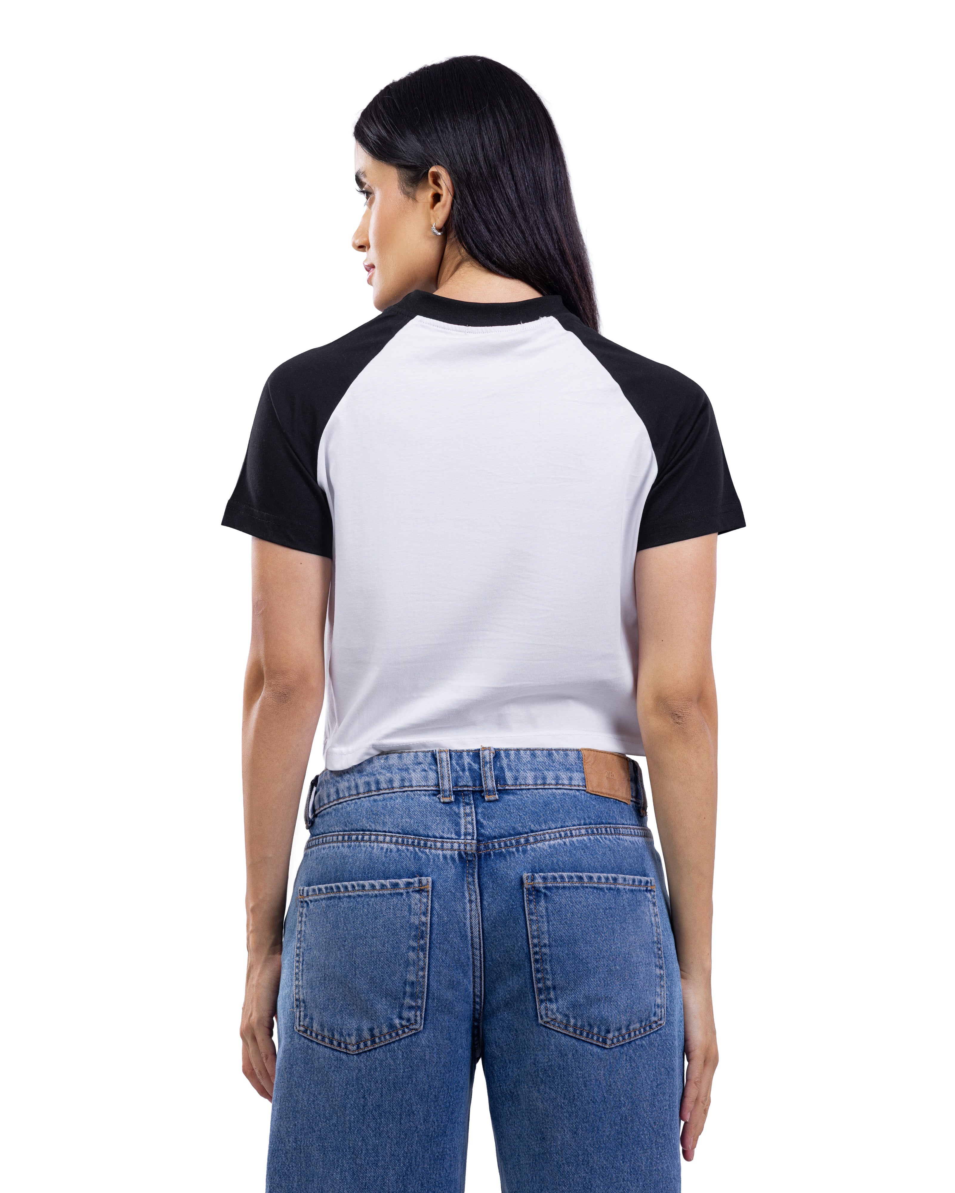 A woman shown from the back wearing a short-sleeve raglan baseball t-shirt with a white body and black sleeves, paired with blue jeans, against a plain white background.