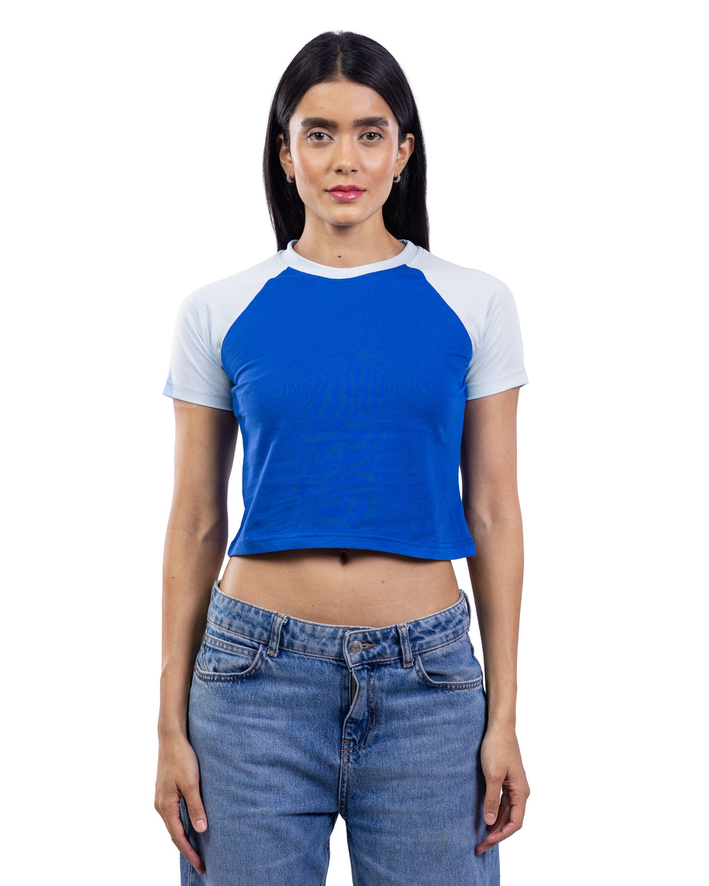 A woman modeling a short-sleeve raglan crop top with a bright blue body and white sleeves, paired with blue jeans, against a plain white background. [model:2]