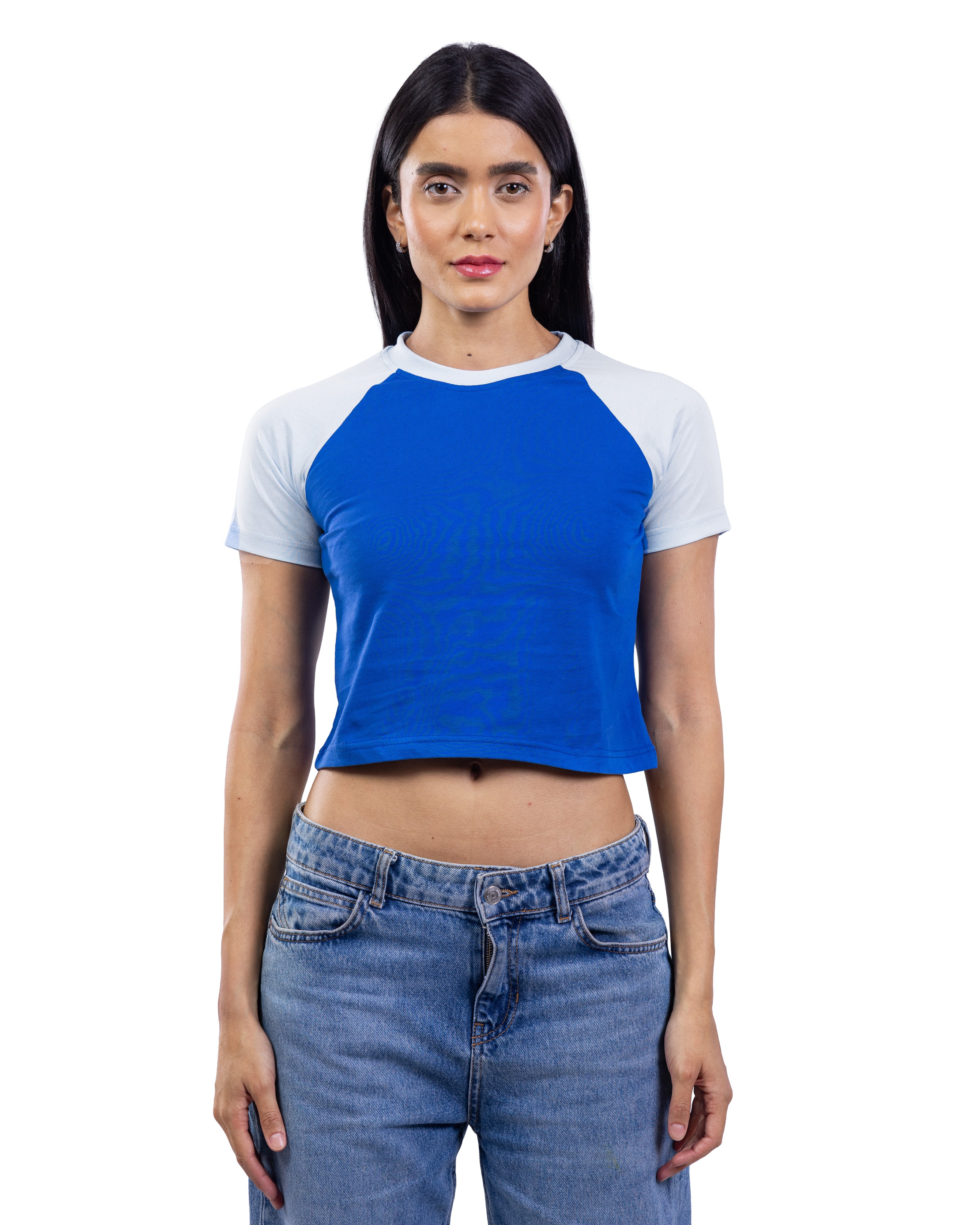 A woman modeling a short-sleeve raglan crop top with a bright blue body and white sleeves, paired with blue jeans, against a plain white background.