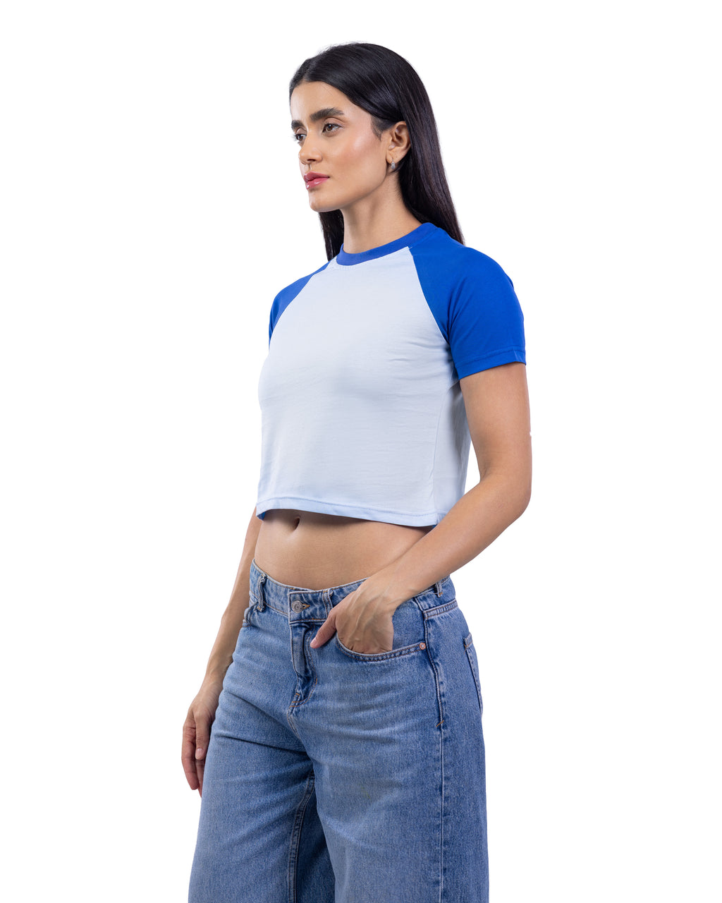 A woman modeling a short-sleeve raglan crop top with a white body and royal blue sleeves, paired with blue jeans, against a plain white background.