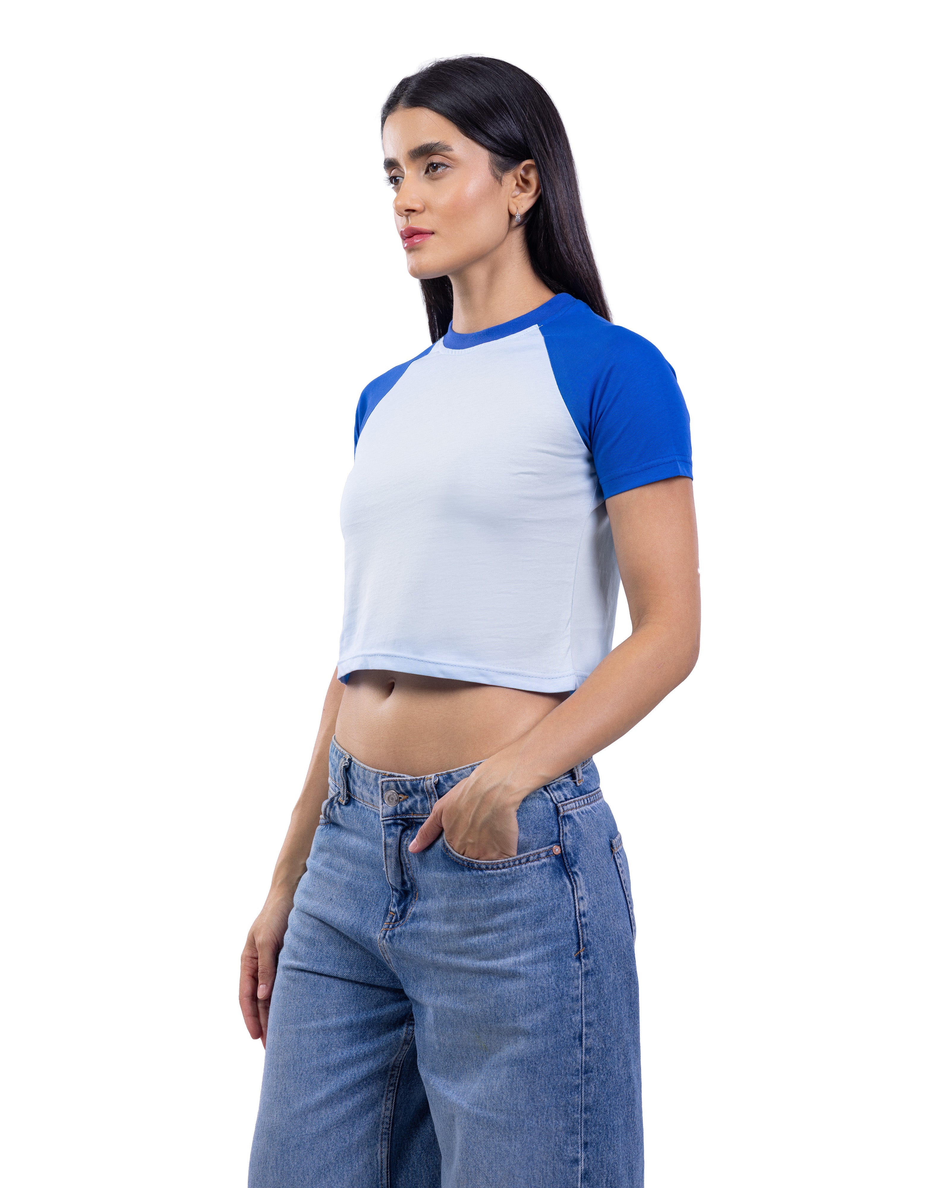 A woman modeling a short-sleeve raglan crop top with a white body and royal blue sleeves, paired with blue jeans, against a plain white background.