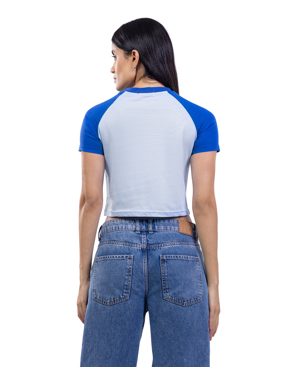 A woman shown from the back wearing a short-sleeve raglan crop top with a light gray body and royal blue sleeves, paired with blue jeans, against a plain white background.