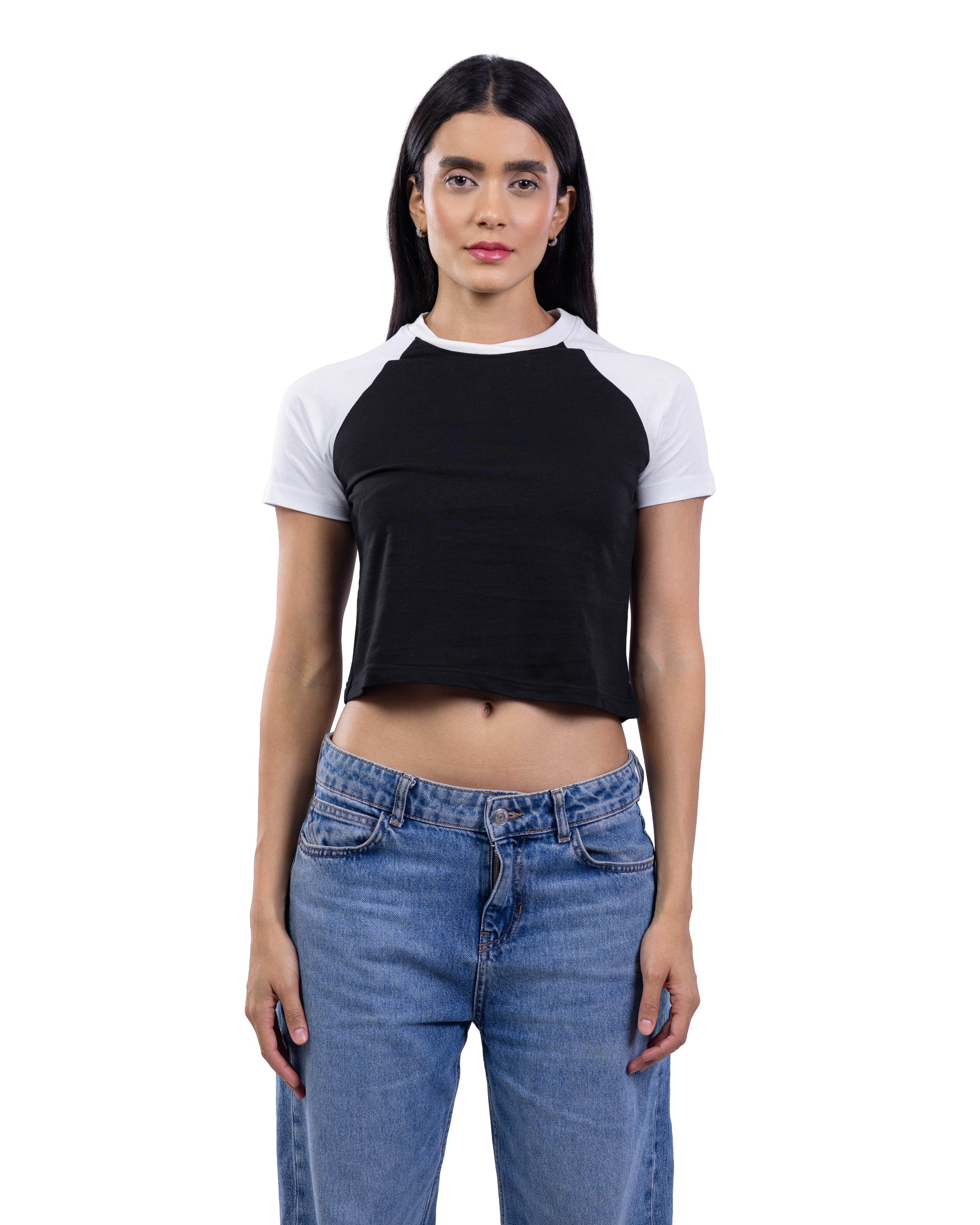 A woman modeling a black and white raglan crop top with blue jeans against a plain white background.