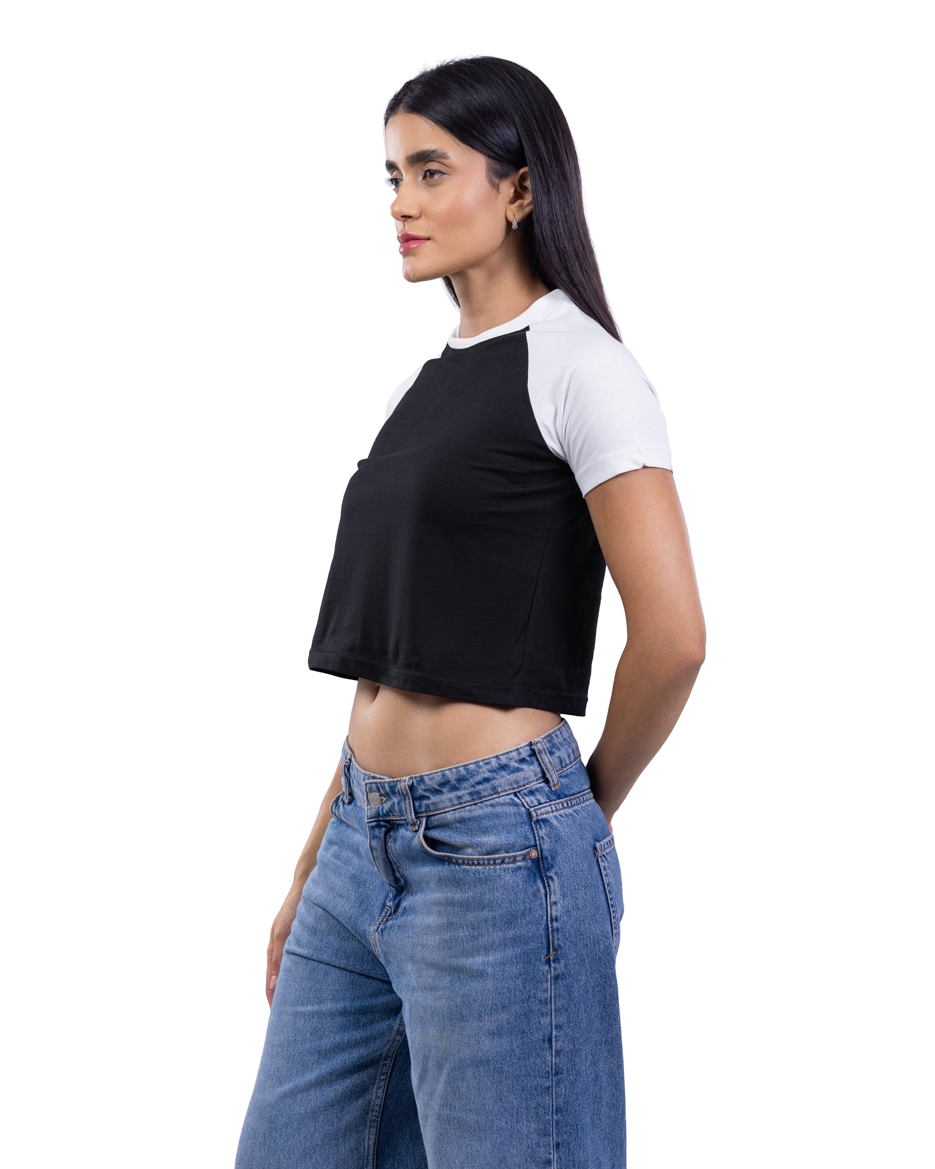 A woman modeling a black and white raglan crop top with blue jeans against a plain white background.