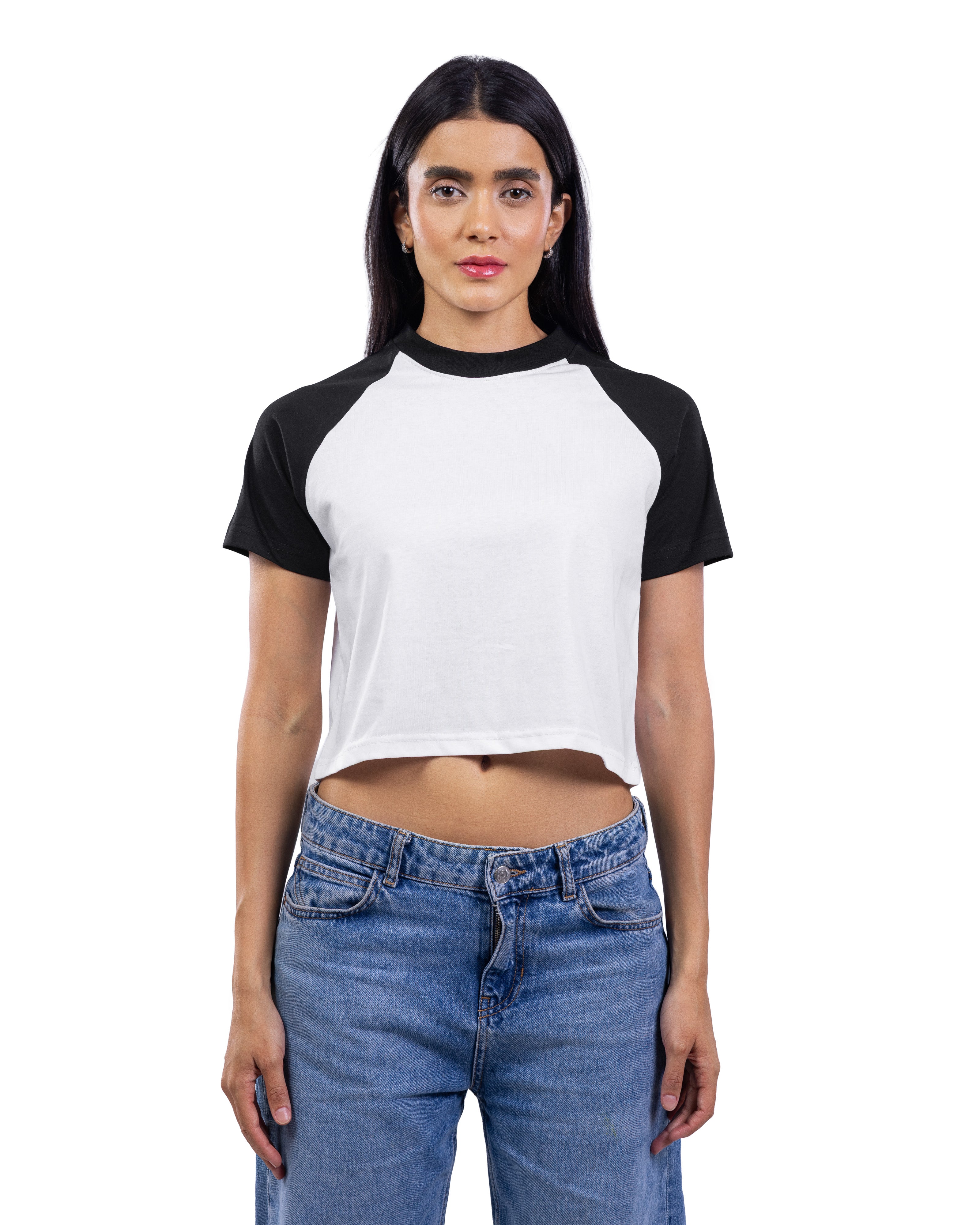 A woman modeling a short-sleeve crop top with a white body and black raglan sleeves, paired with blue jeans, against a plain white background.