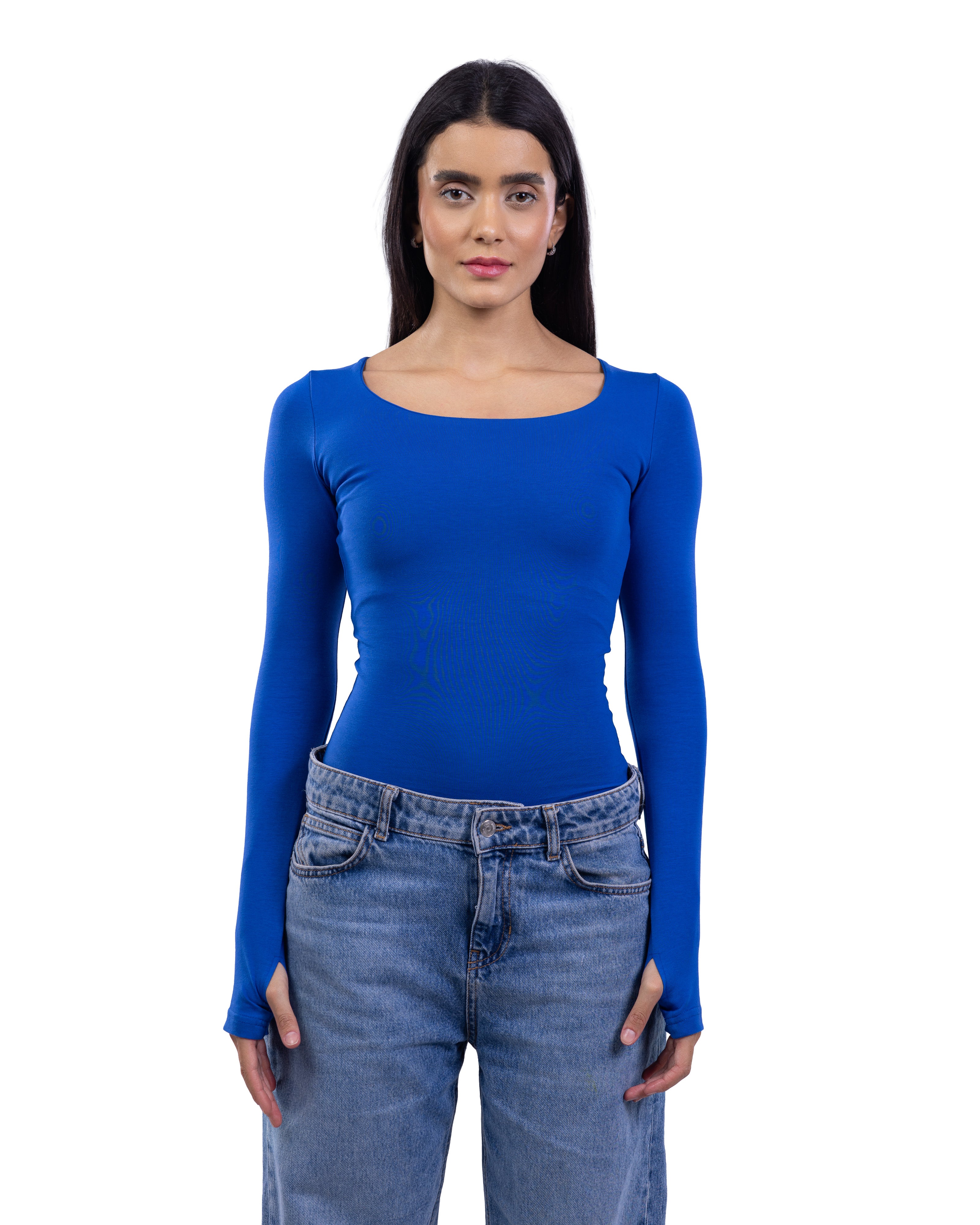 A woman modeling a royal blue long-sleeve scoop-neck top paired with light-wash blue jeans, standing against a solid white background.