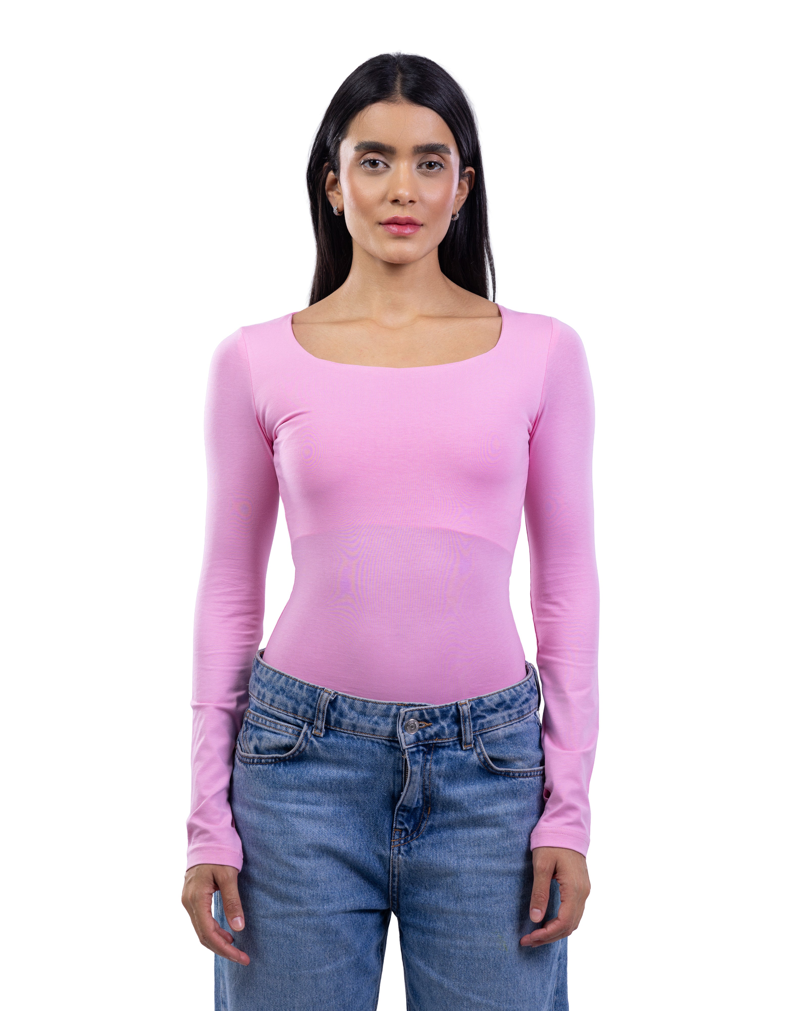A woman modeling a light pink long-sleeve scoop-neck top paired with blue jeans, shot against a solid white background.