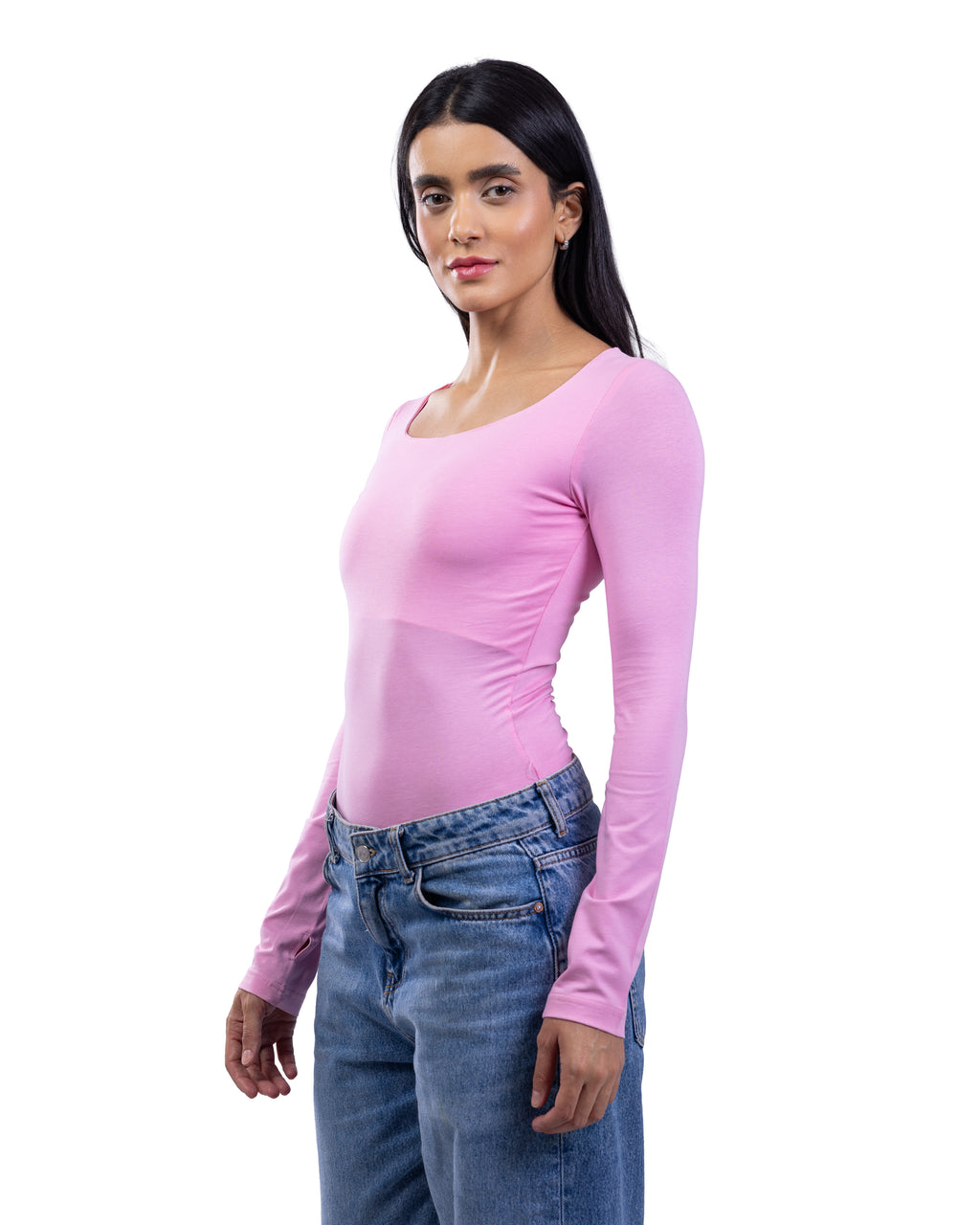 A woman modeling a fitted, long-sleeve scoop-neck top in light pink, paired with blue jeans, against a plain white background.