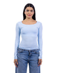 A woman modeling a light blue long-sleeve scoop-neck top paired with blue jeans, shot against a solid white background.