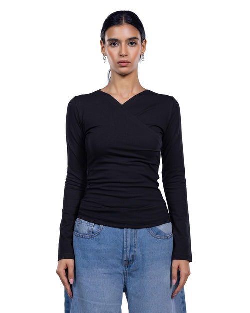 A woman modeling a black long-sleeve wrap-style top with a V-neckline, paired with light blue jeans, against a plain white background.