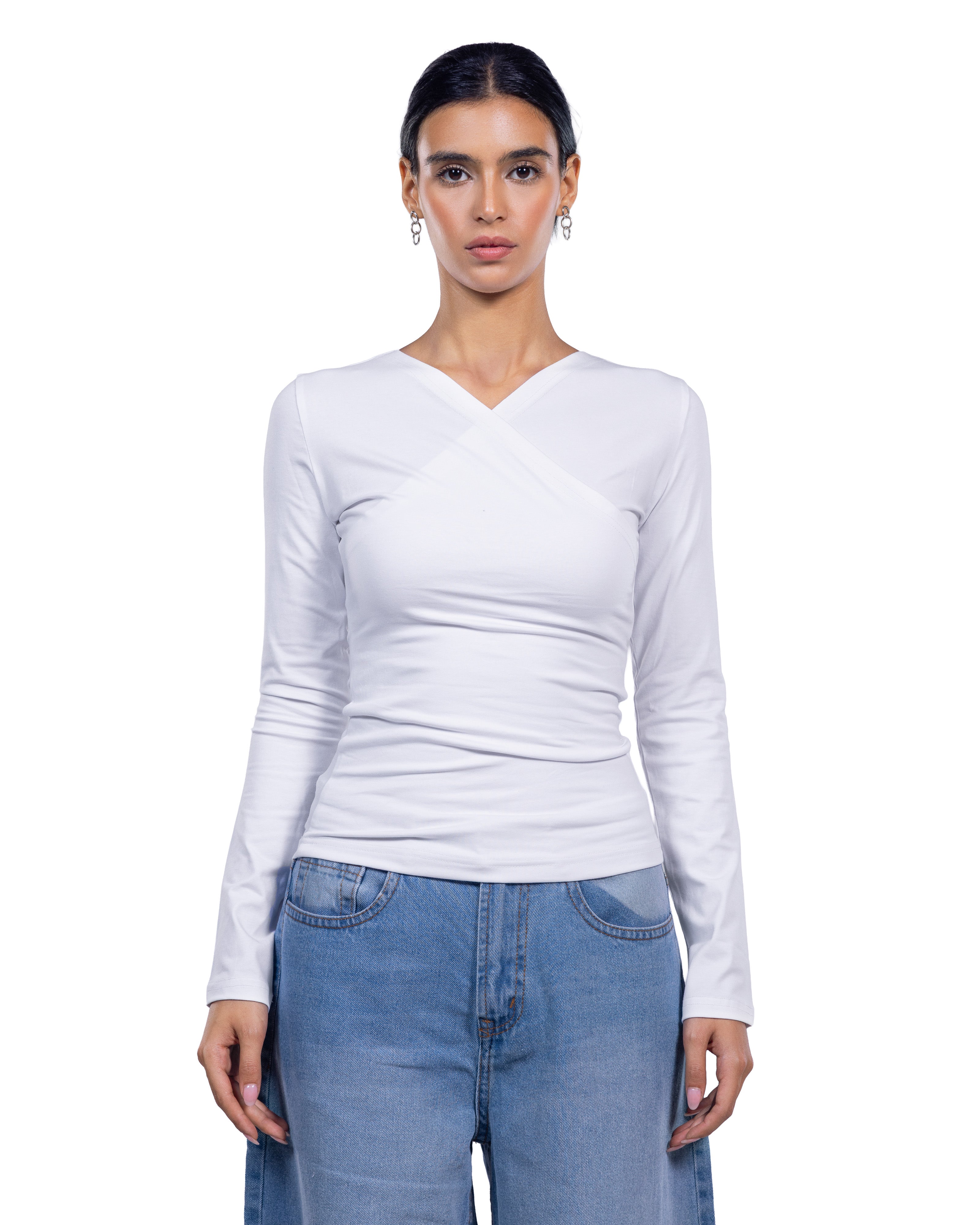 A woman modeling a fitted white long-sleeve top with a crossover V-neck design, paired with light blue jeans, against a plain white background.