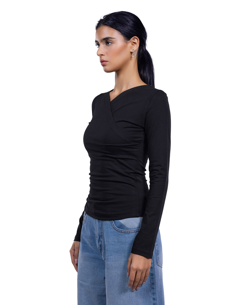 A woman wearing a fitted black long-sleeve wrap-style top and light blue jeans, shown in side profile against a plain white background.