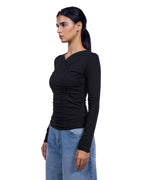 A woman wearing a fitted black long-sleeve wrap-style top and light blue jeans, shown in side profile against a plain white background. [model:1]