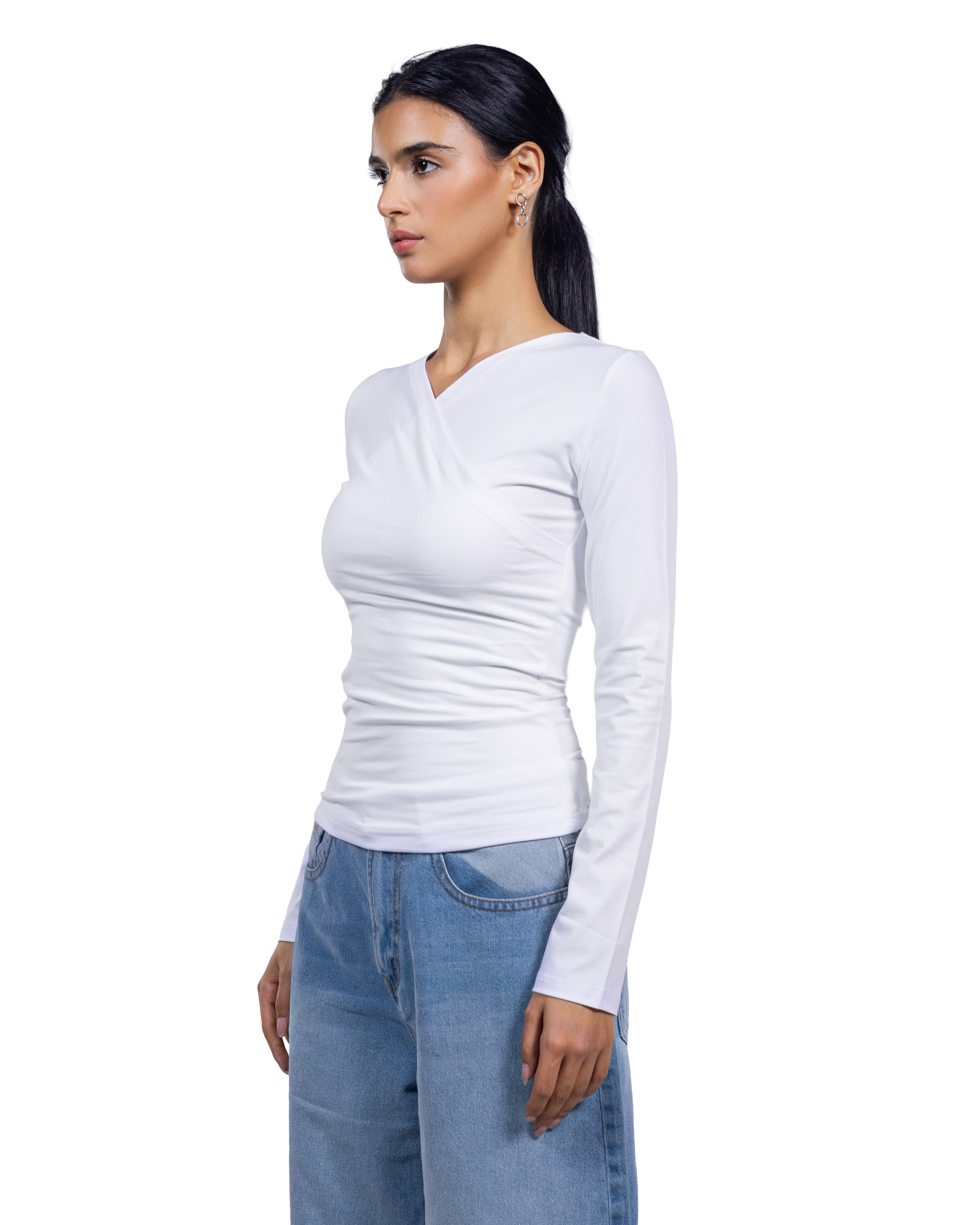 A woman wearing a fitted white long-sleeve top with a wrap-style V-neck and light blue jeans, shown in profile against a plain white background.