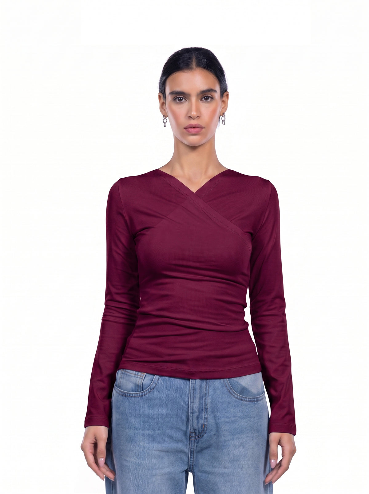 A woman modeling a long-sleeve wrap-style top in deep burgundy, paired with light blue jeans, against a plain white background.