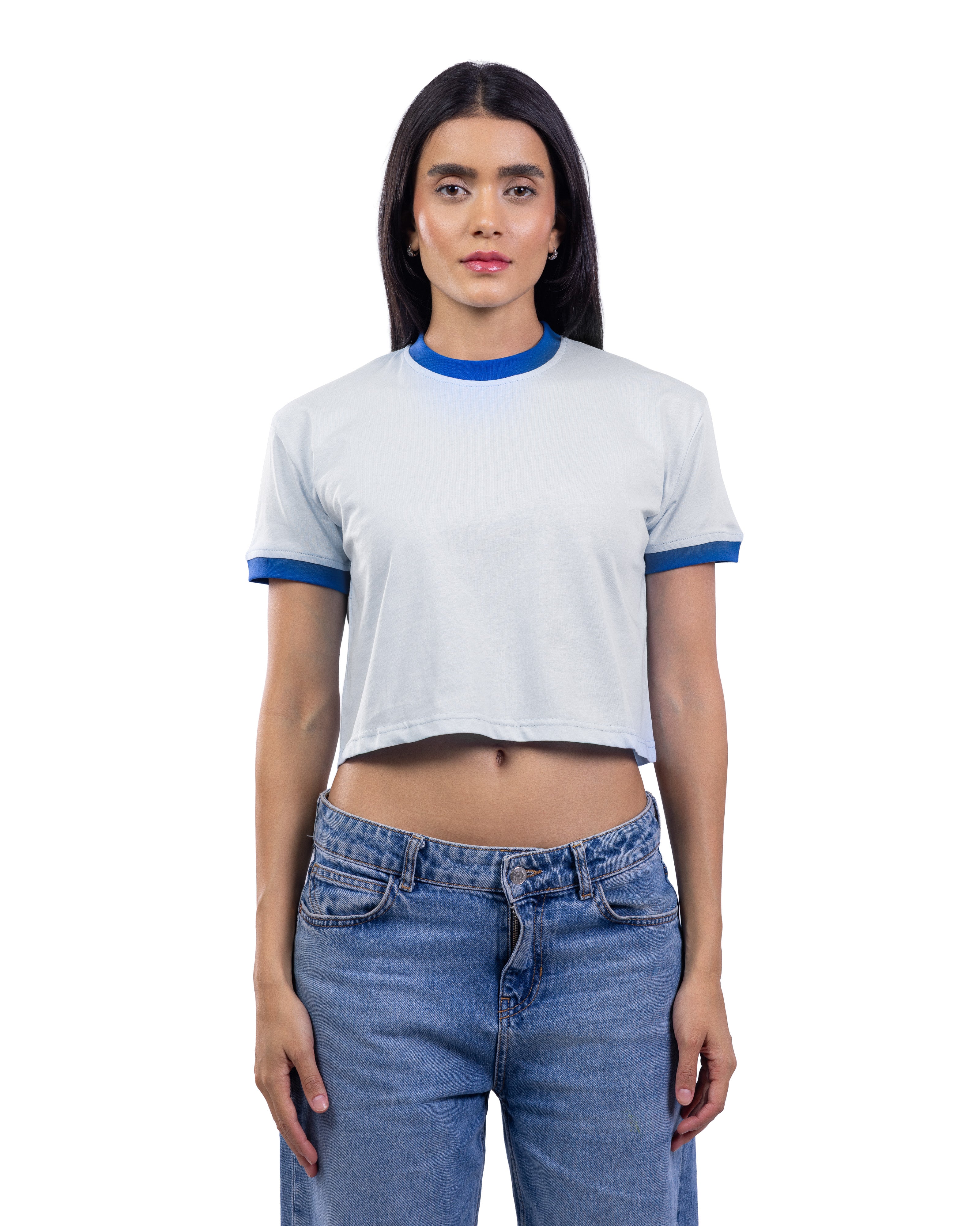A woman modeling a white cropped ringer t-shirt with blue trim on the collar and sleeve cuffs, paired with blue jeans, against a plain white background.
