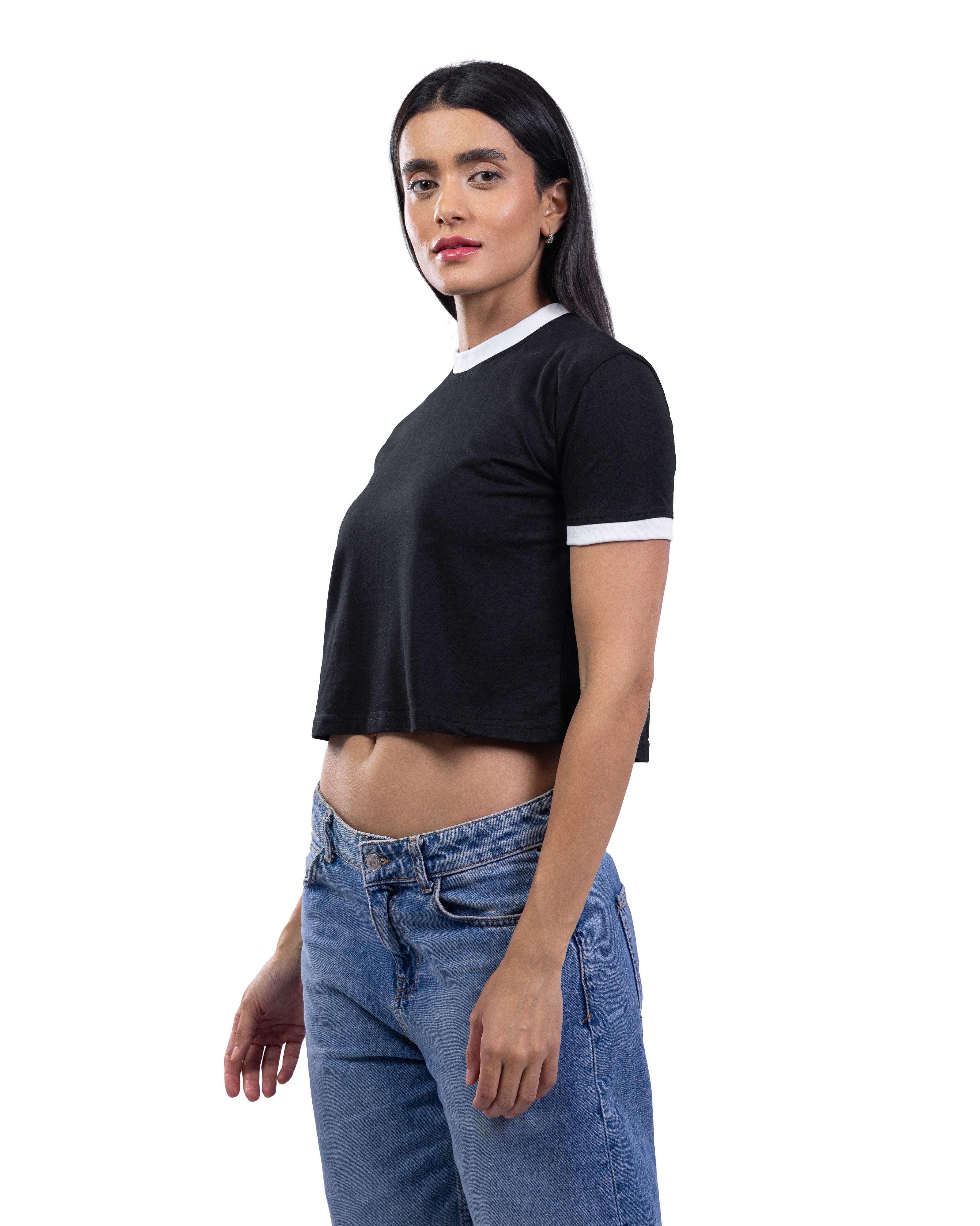 A woman modeling a black short-sleeve crop top with white ribbed trim at the crew neck and sleeve cuffs, paired with blue jeans, against a plain white background.