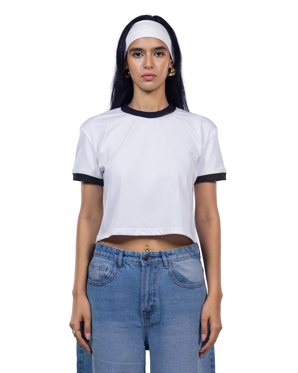 A woman modeling a white cropped ringer T-shirt with black trim on the collar and sleeve cuffs, paired with light blue jeans and a white headband, against a plain white background.