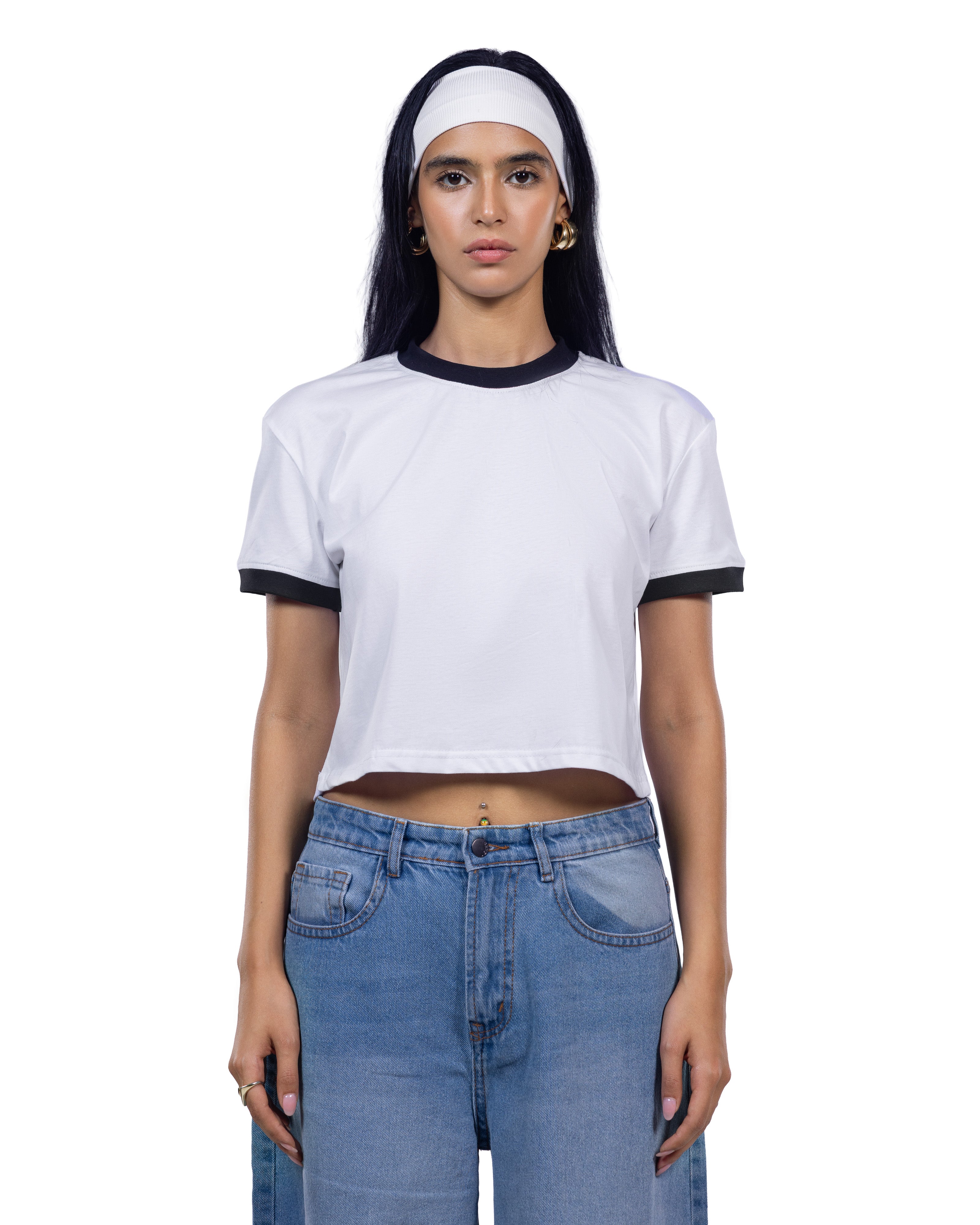 A woman modeling a white cropped ringer T-shirt with black trim on the collar and sleeve cuffs, paired with light blue jeans and a white headband, against a plain white background.