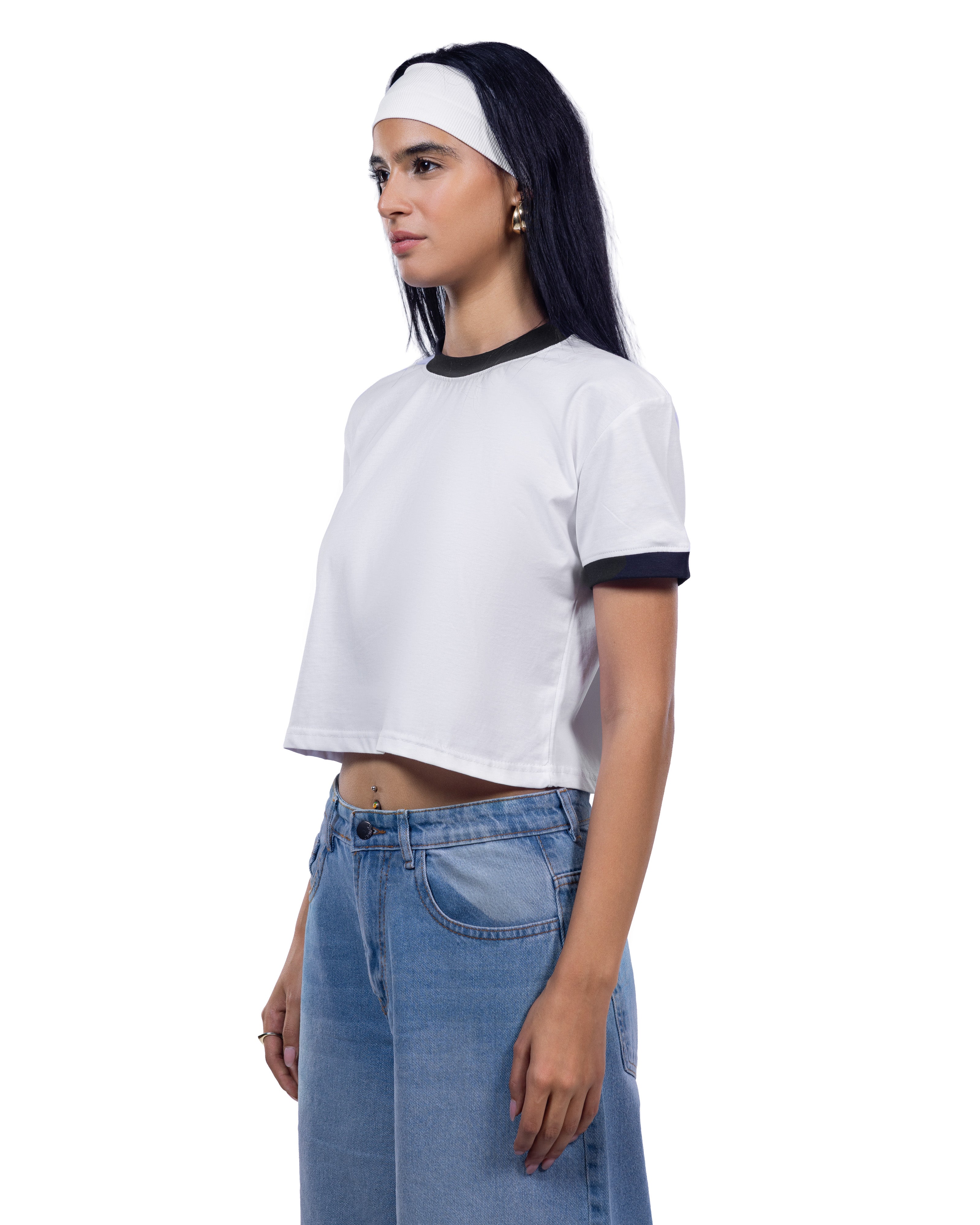 A woman wearing a white cropped ringer t-shirt with black trim on the collar and sleeve cuffs, paired with light blue jeans and a white headband, shown from a side profile against a plain white background.