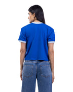 A woman shown from the back wearing a bright blue short-sleeve ringer T-shirt with white trim on the collar and sleeve cuffs, paired with blue jeans, against a plain white background. [model:2]