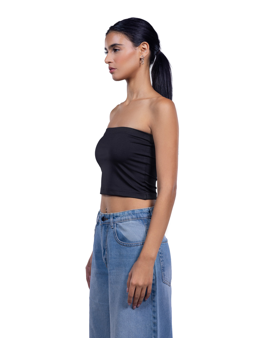A woman in side profile wearing a black strapless tube crop top and light blue denim jeans against a plain white background.