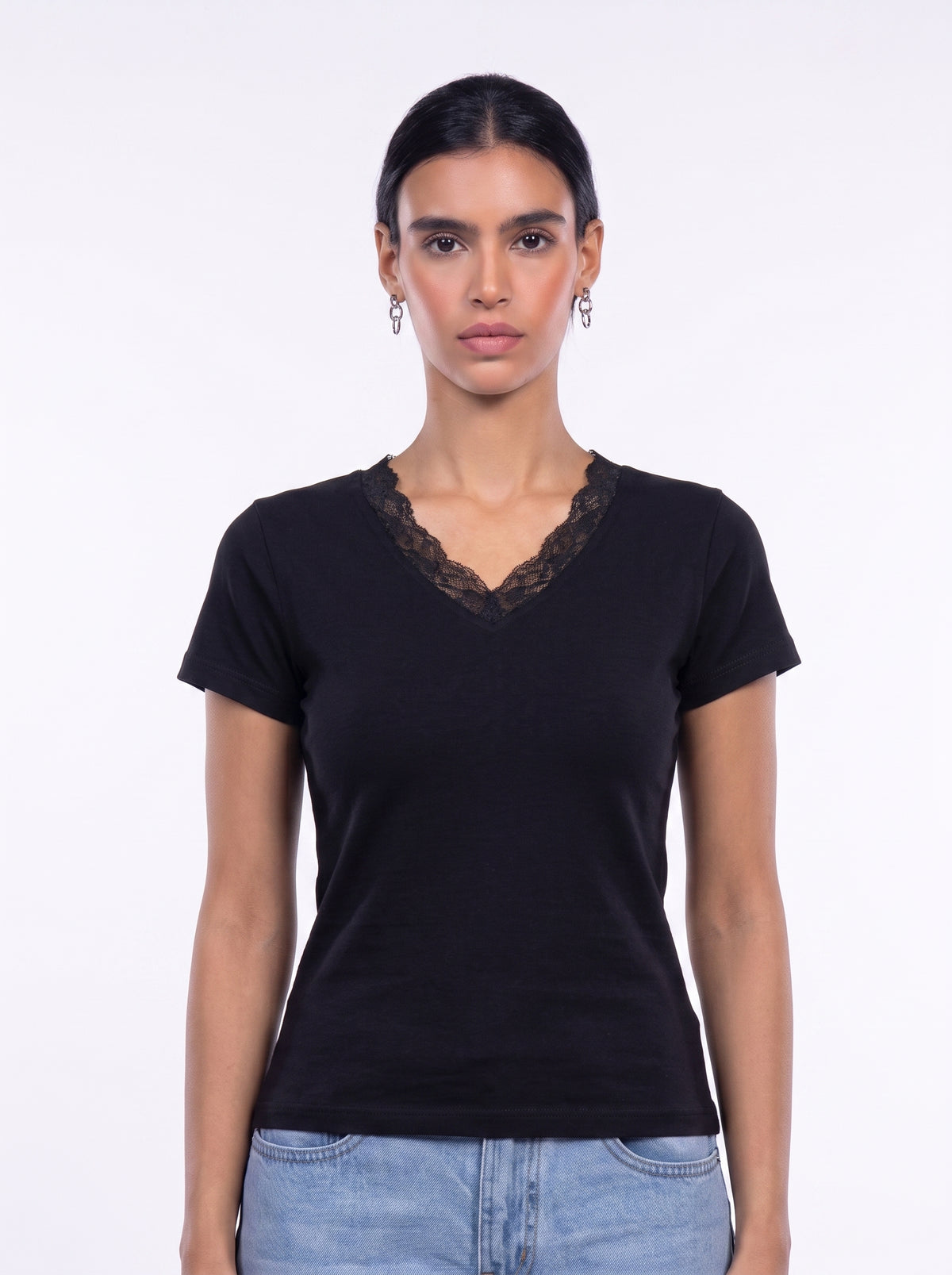 A woman modeling a black short-sleeve V-neck t-shirt with a black lace trim along the neckline, paired with light blue jeans, against a plain white studio background.