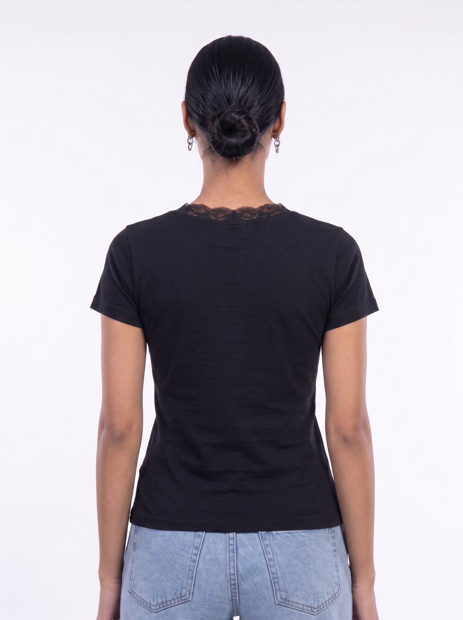 A woman viewed from the back wearing a black short-sleeve t-shirt with a lace-trimmed neckline and light blue jeans, set against a plain white studio background.