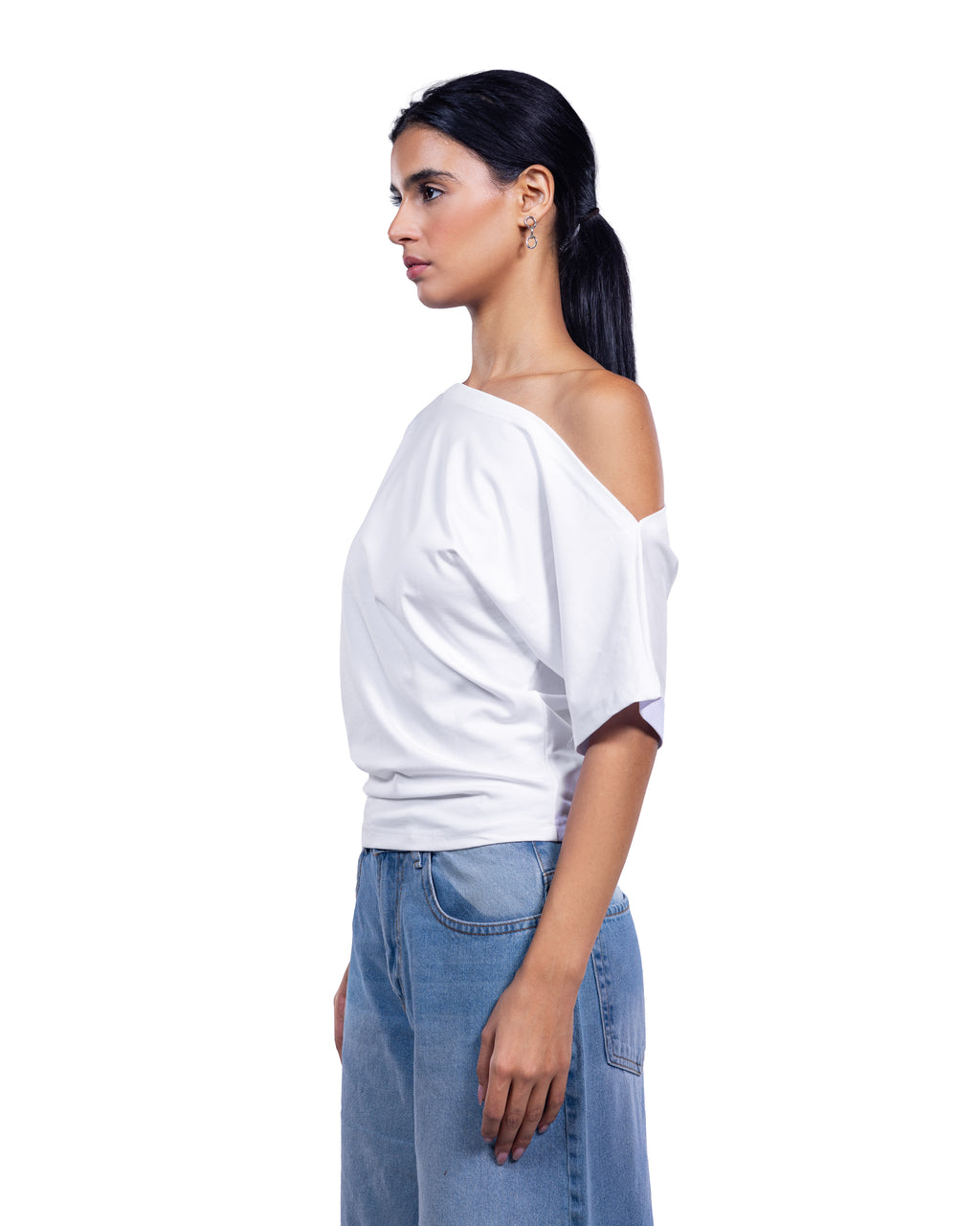 A woman shown in side profile wearing a white off-the-shoulder short-sleeve top and light blue jeans against a plain white studio background.