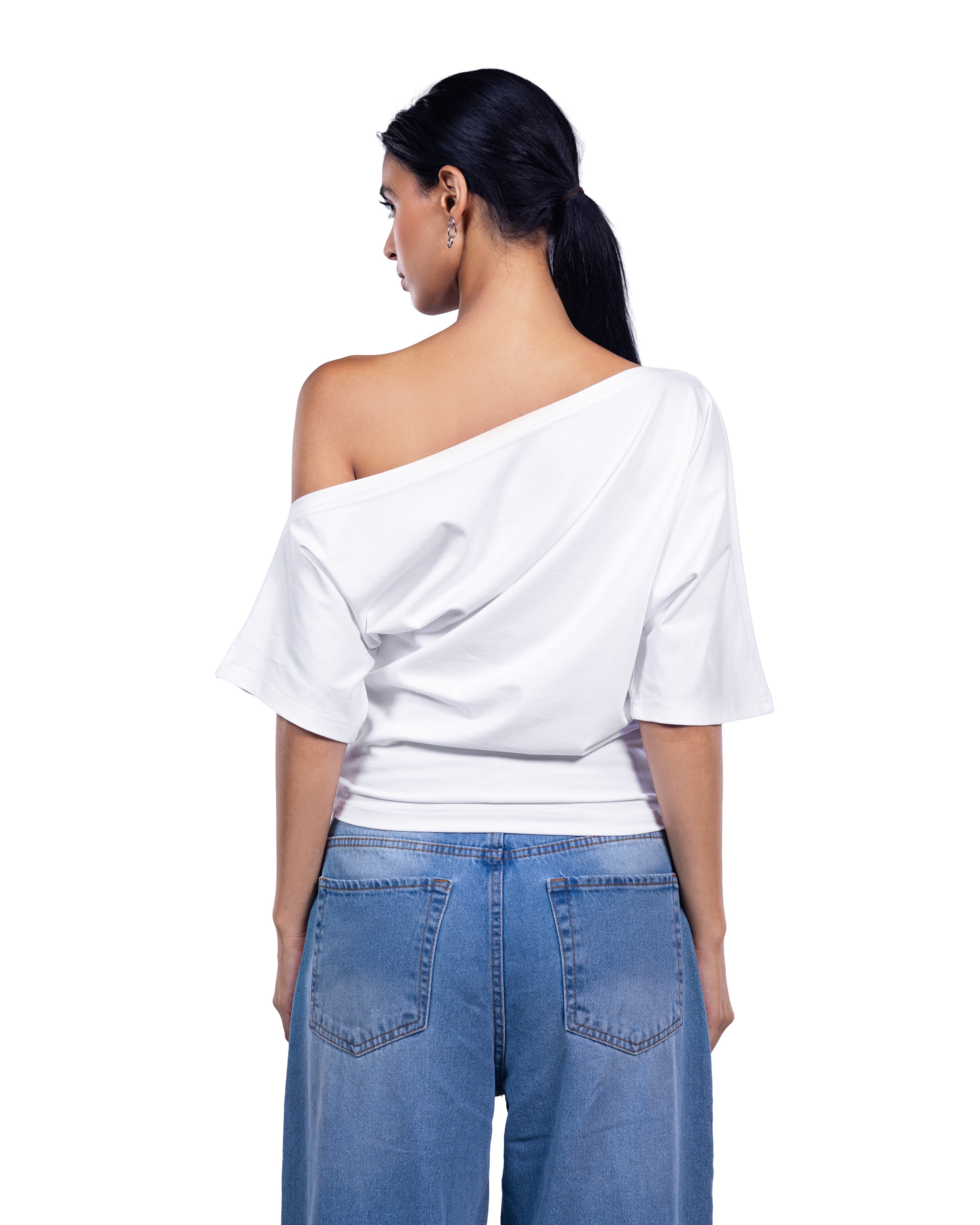 A woman shown from the back wearing a white draped off-the-shoulder top and blue jeans against a plain white background.