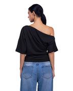 A woman shown from the back wearing a black off-the-shoulder draped top and light blue jeans against a plain white background. [model:1]