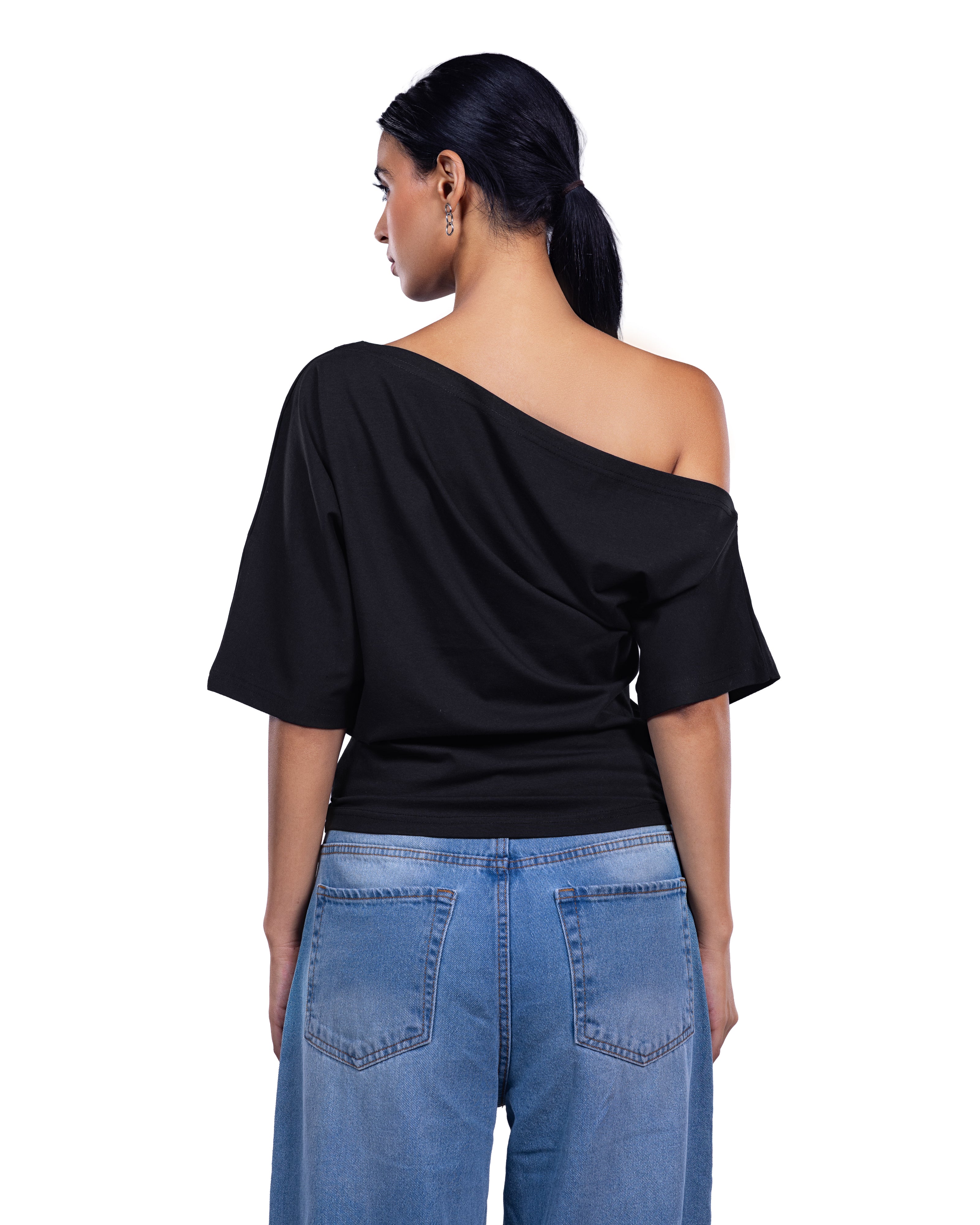 A woman shown from the back wearing a black off-the-shoulder draped top and light blue jeans against a plain white background.
