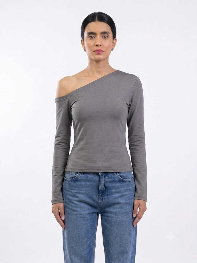 A woman modeling a long-sleeve, asymmetrical one-shoulder top in a medium gray color, paired with blue jeans, against a plain white studio background.