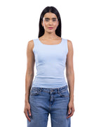 A woman modeling a light blue scoop-neck tank top paired with blue jeans, shot against a solid white background.