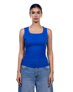 A woman modeling a bright royal blue sleeveless tank top with a square neckline, paired with light blue jeans, against a plain white background.