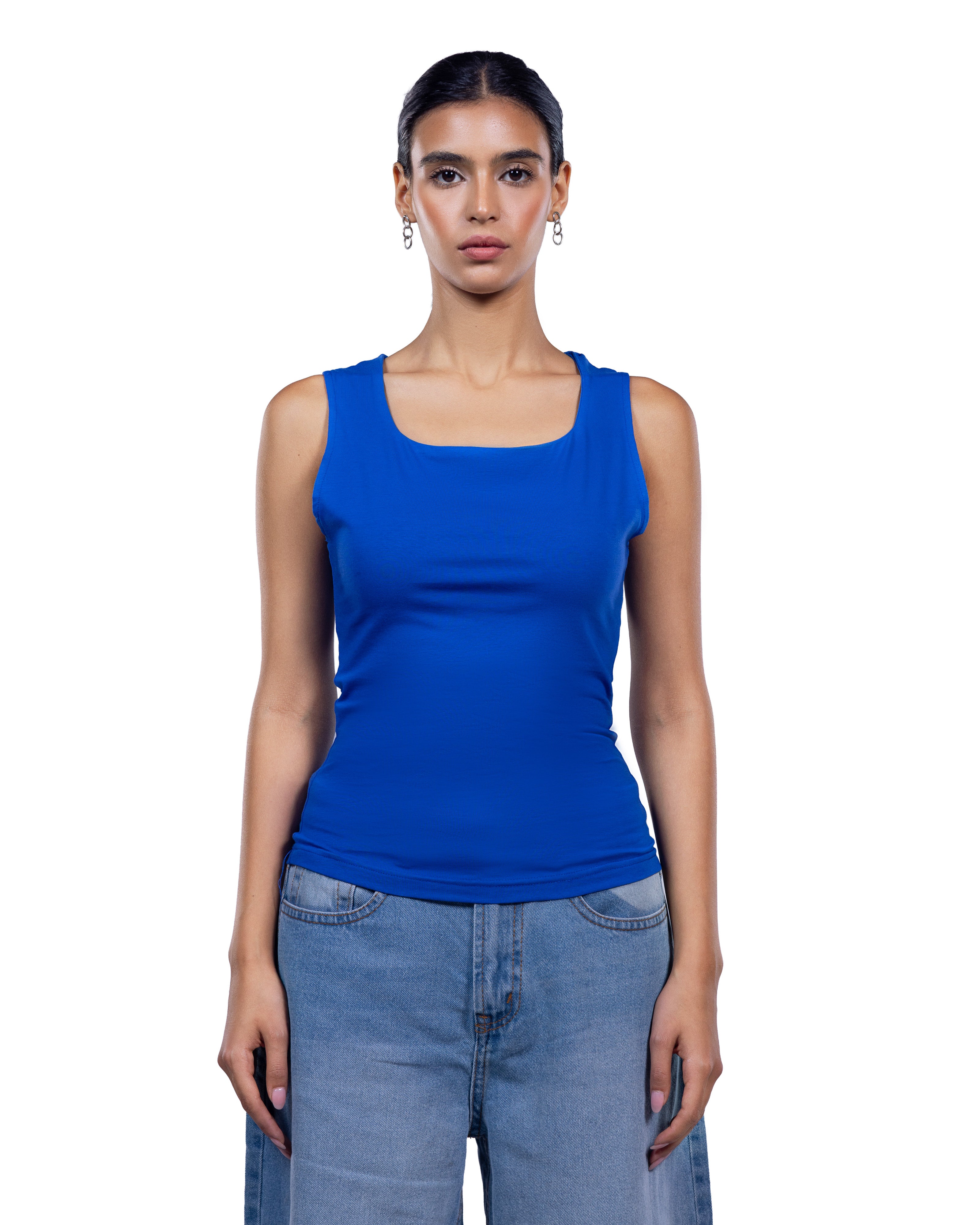 A woman modeling a bright royal blue sleeveless tank top with a square neckline, paired with light blue jeans, against a plain white background.
