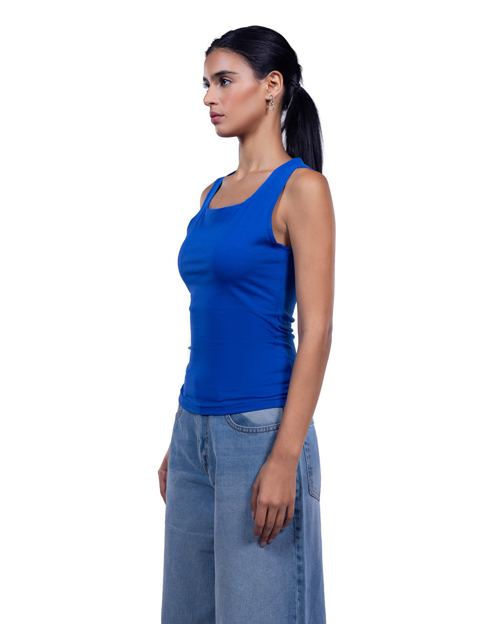 A woman in side profile wearing a bright royal blue scoop-neck tank top and light-wash blue jeans, standing against a plain white background.