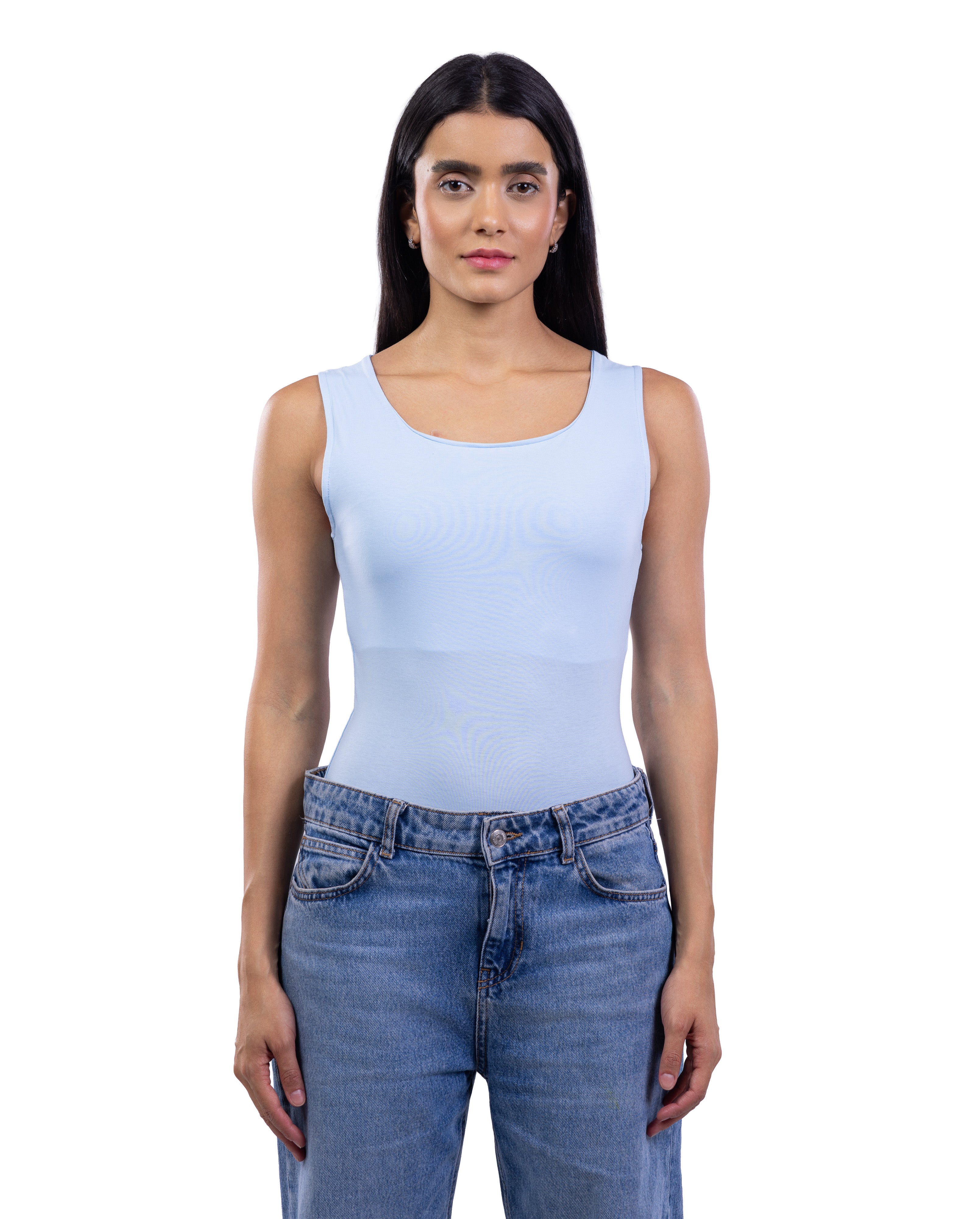 A woman modeling a light blue sleeveless bodysuit or tank top paired with blue jeans, shot against a solid white background.