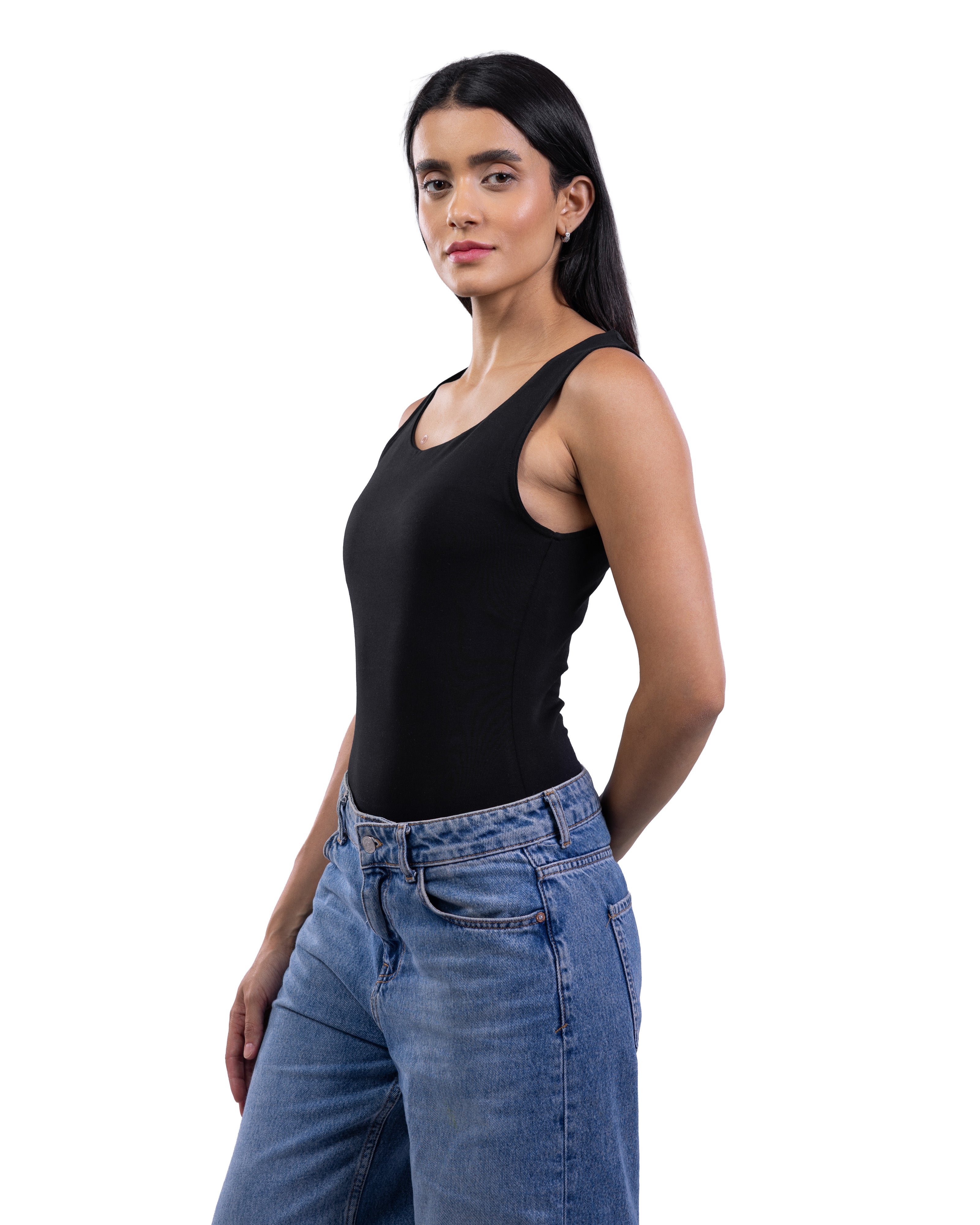 A woman modeling a black sleeveless scoop-neck tank top paired with blue jeans, photographed against a solid white background.