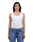 A woman modeling a white sleeveless scoop-neck tank top paired with blue jeans, shot against a solid white background.